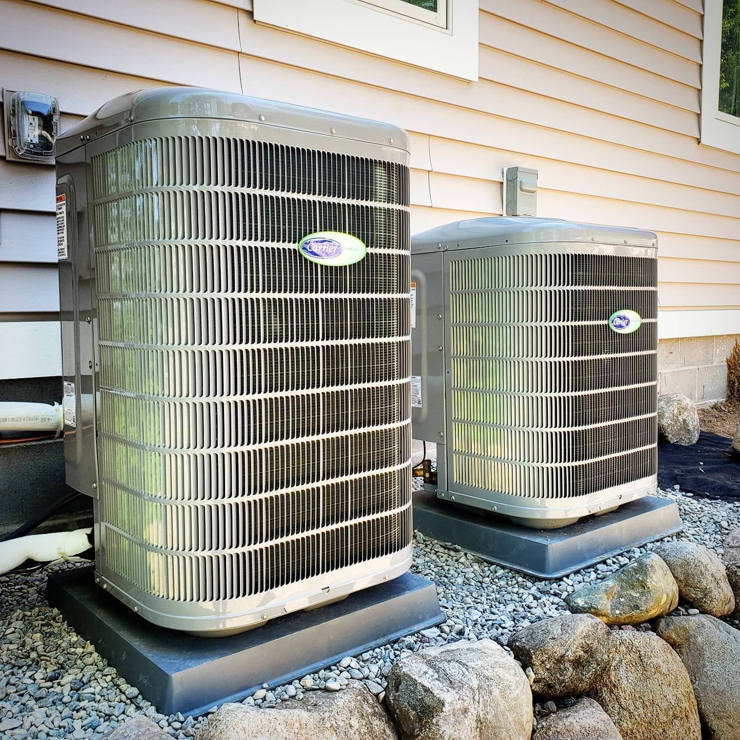 Two air conditioners are sitting outside of a house.