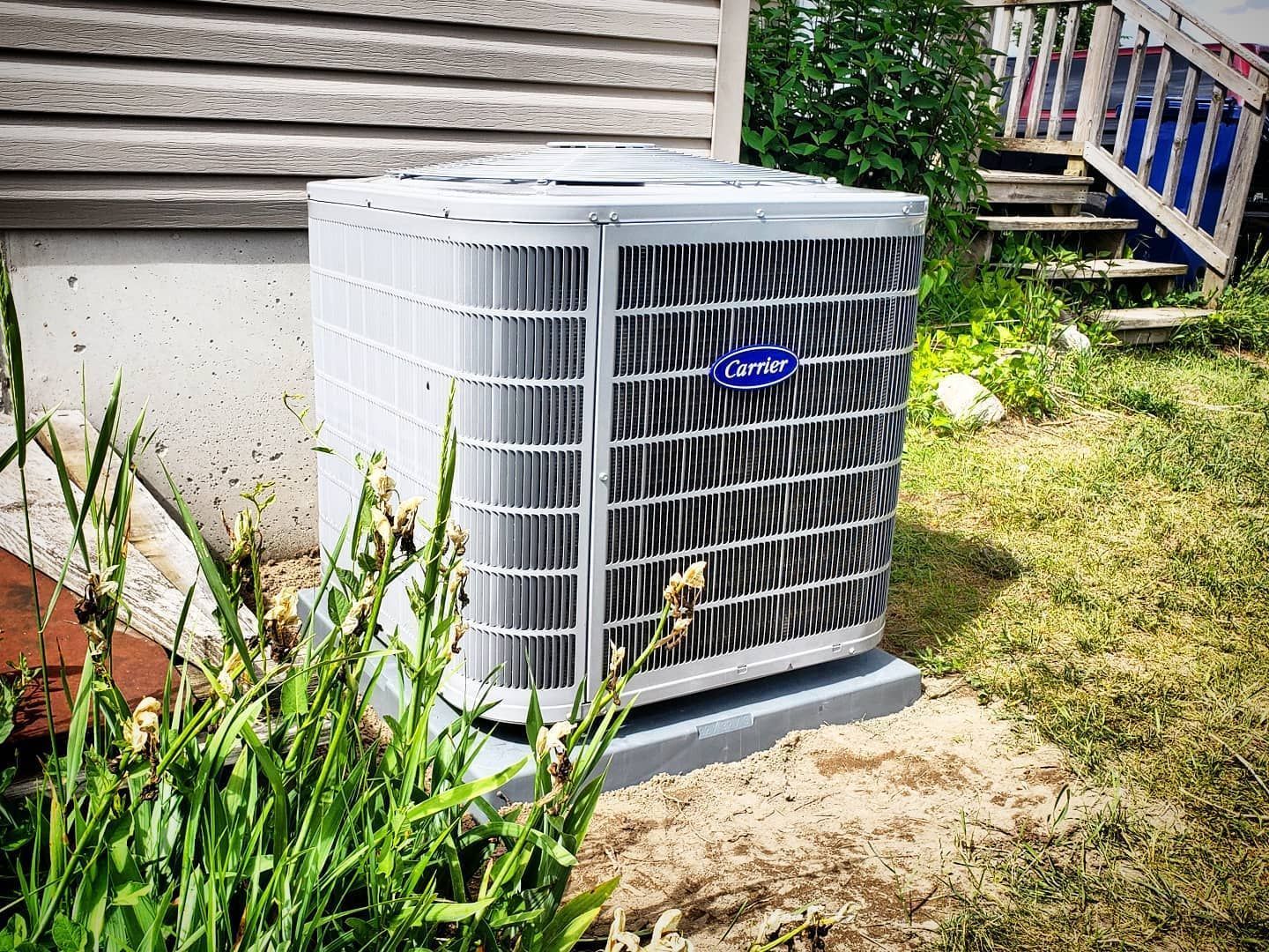 A carrier air conditioner is sitting in the grass in front of a house.