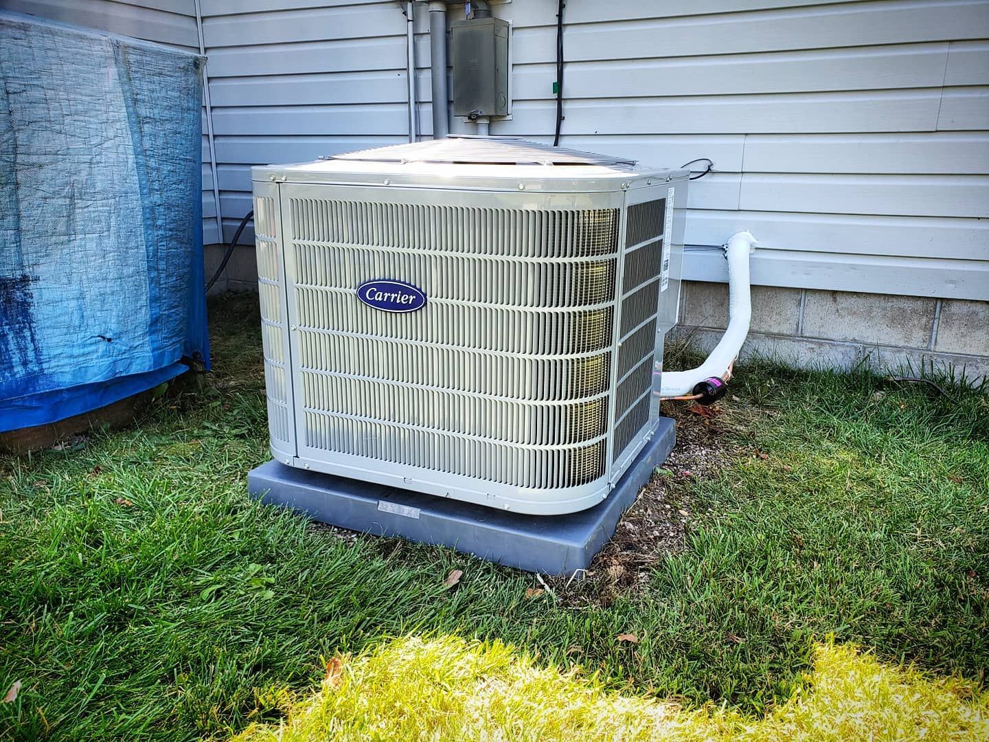 A carrier air conditioner is sitting in the grass next to a house.