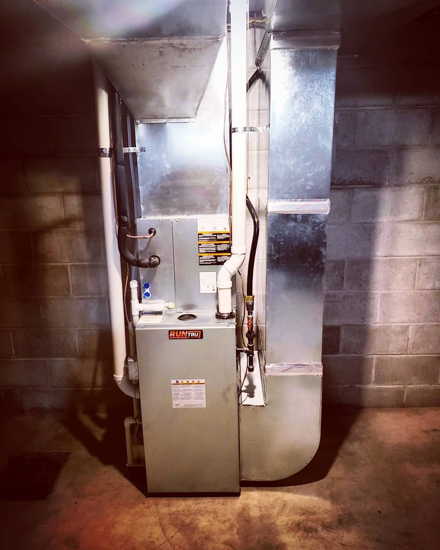 An air conditioner is sitting in a basement next to a brick wall.