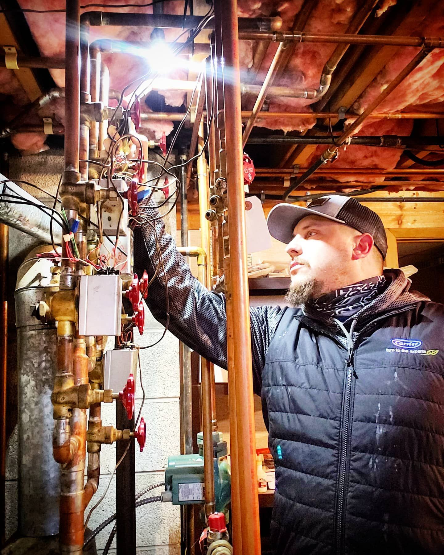 A man is working on a pipe system in a basement.