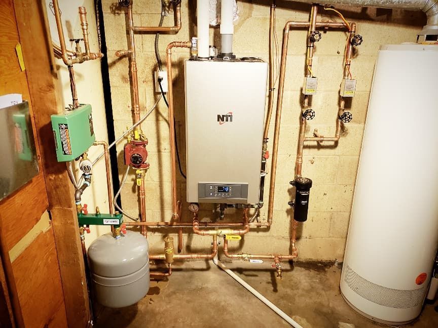 A boiler is sitting in a basement next to a water heater.