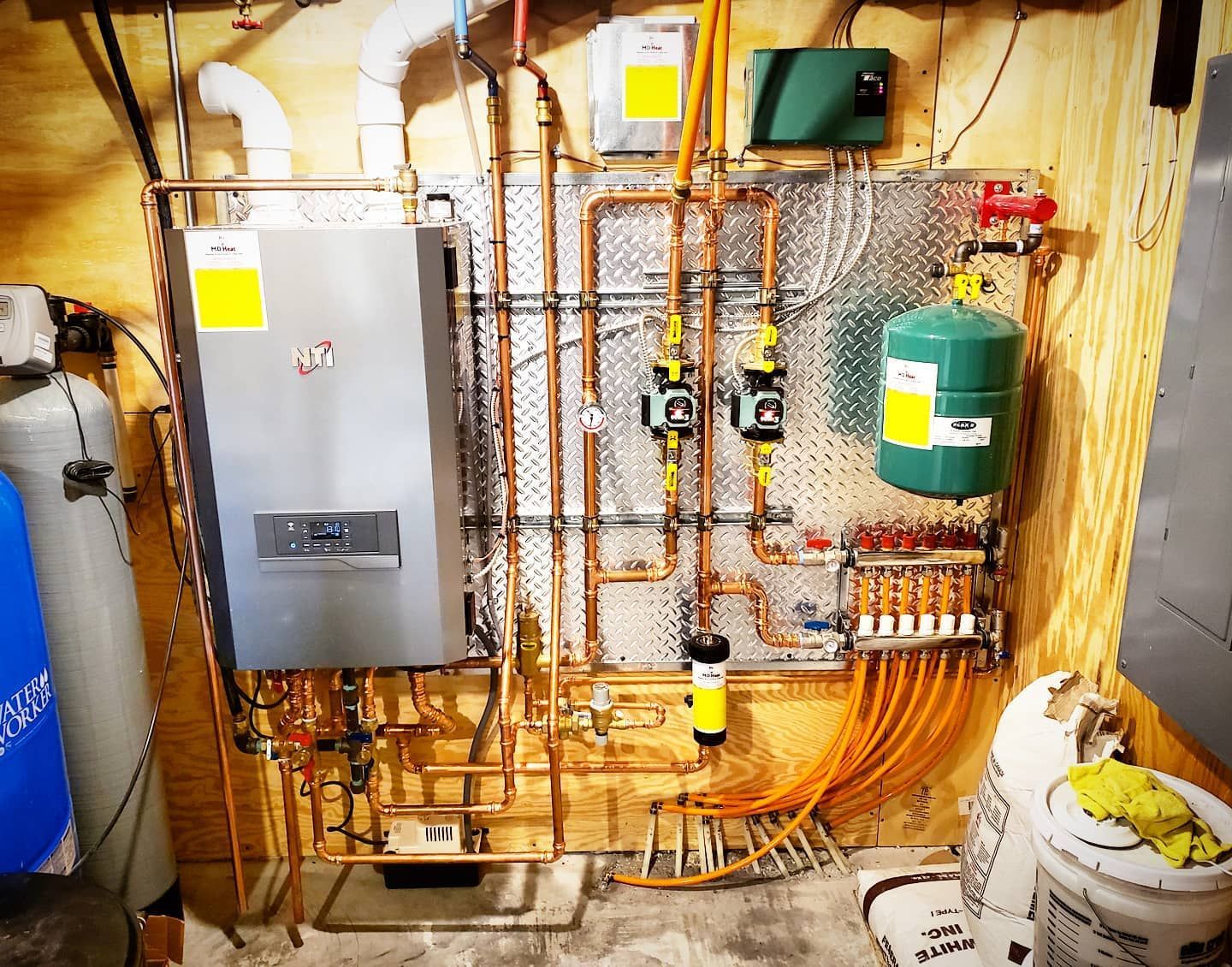 A room with a lot of pipes and a boiler on the wall.