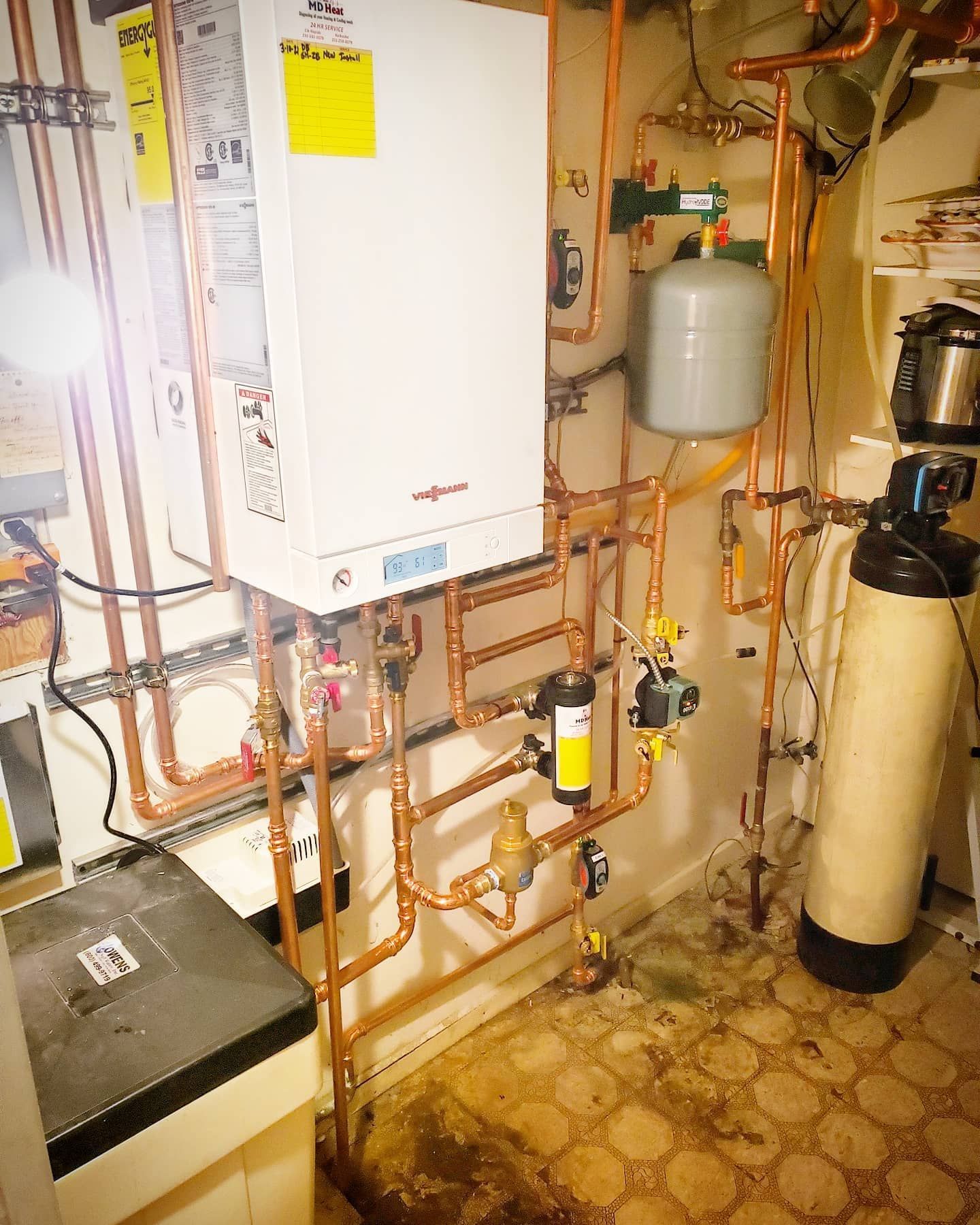 A room with a lot of pipes and a boiler on the wall.