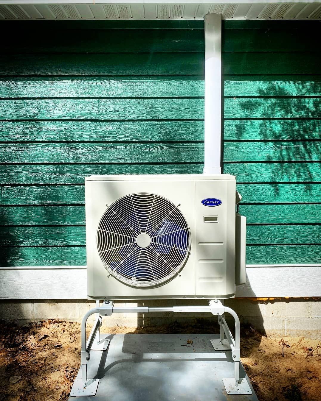 A white air conditioner is sitting outside of a green house.