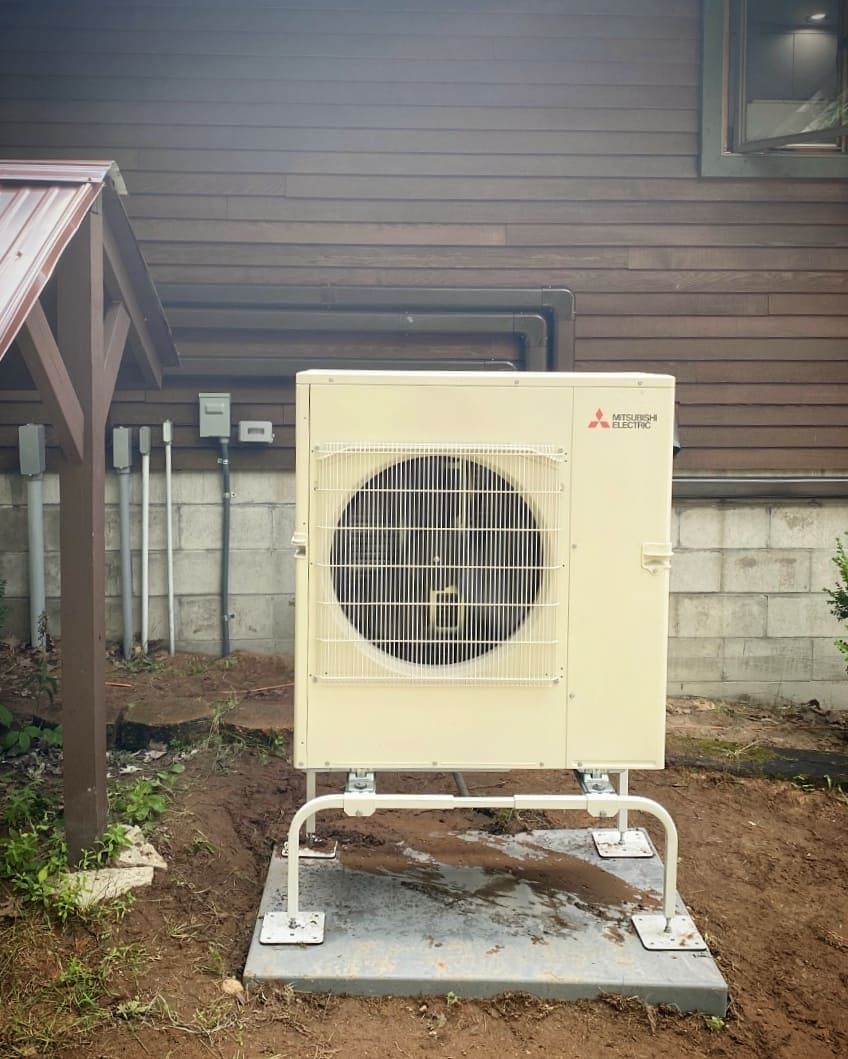 A large air conditioner is sitting on top of a concrete platform in front of a house.