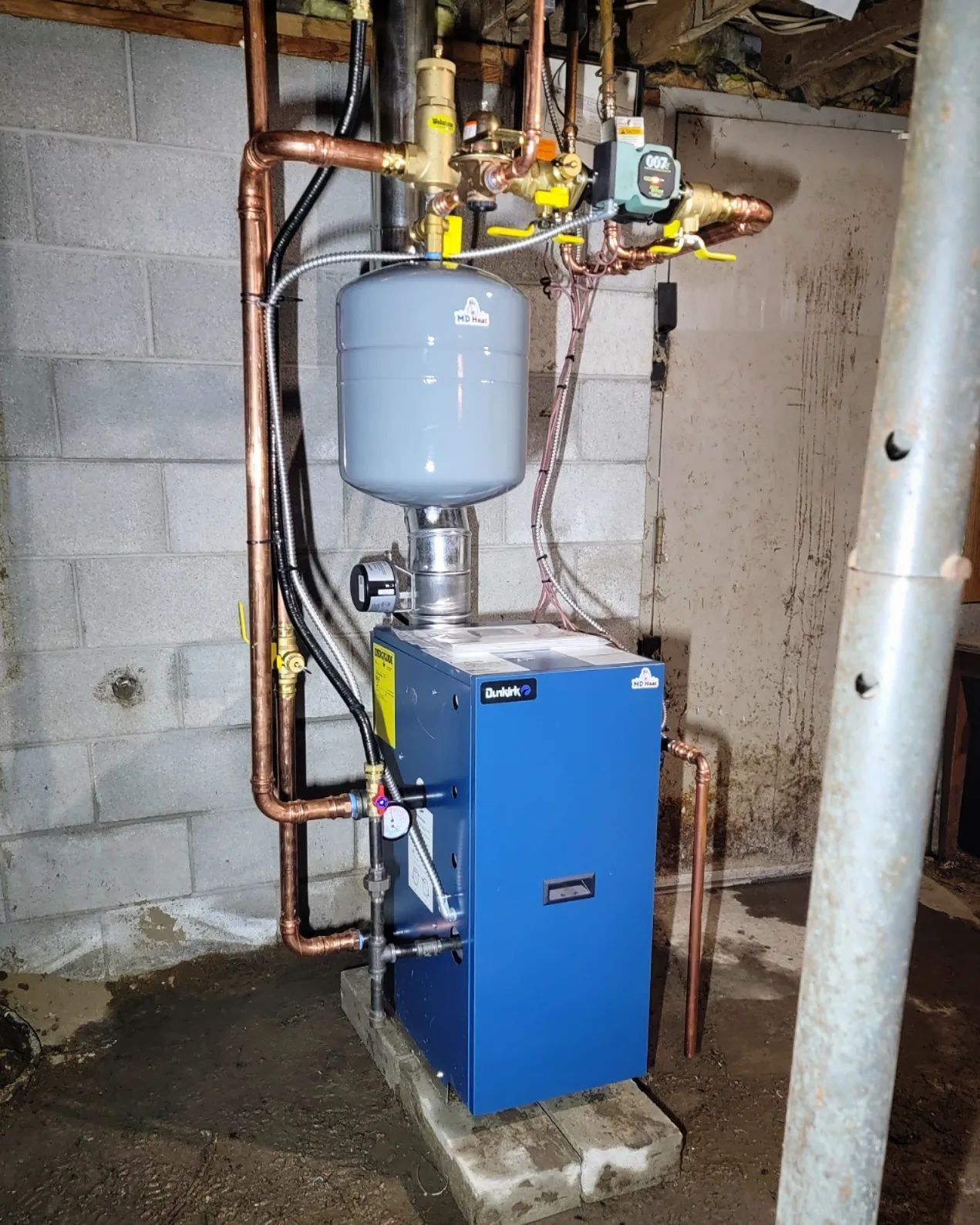 A blue boiler is sitting in a basement next to a brick wall.
