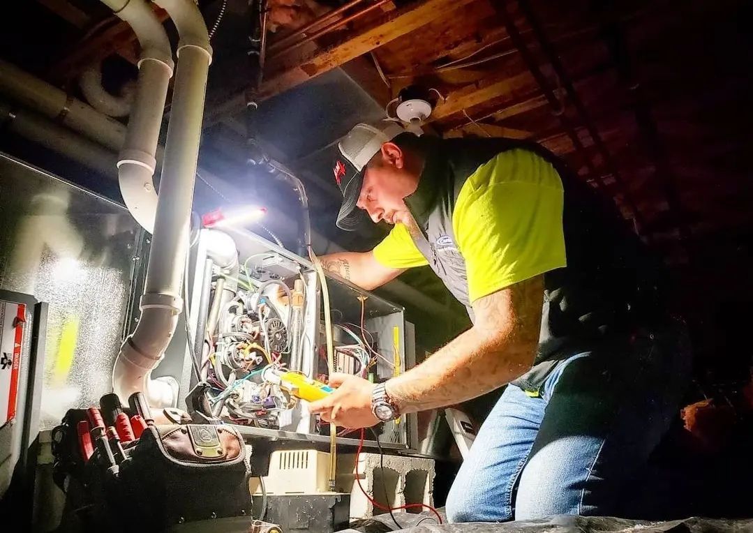 A man is working on an air conditioner in a basement at night.