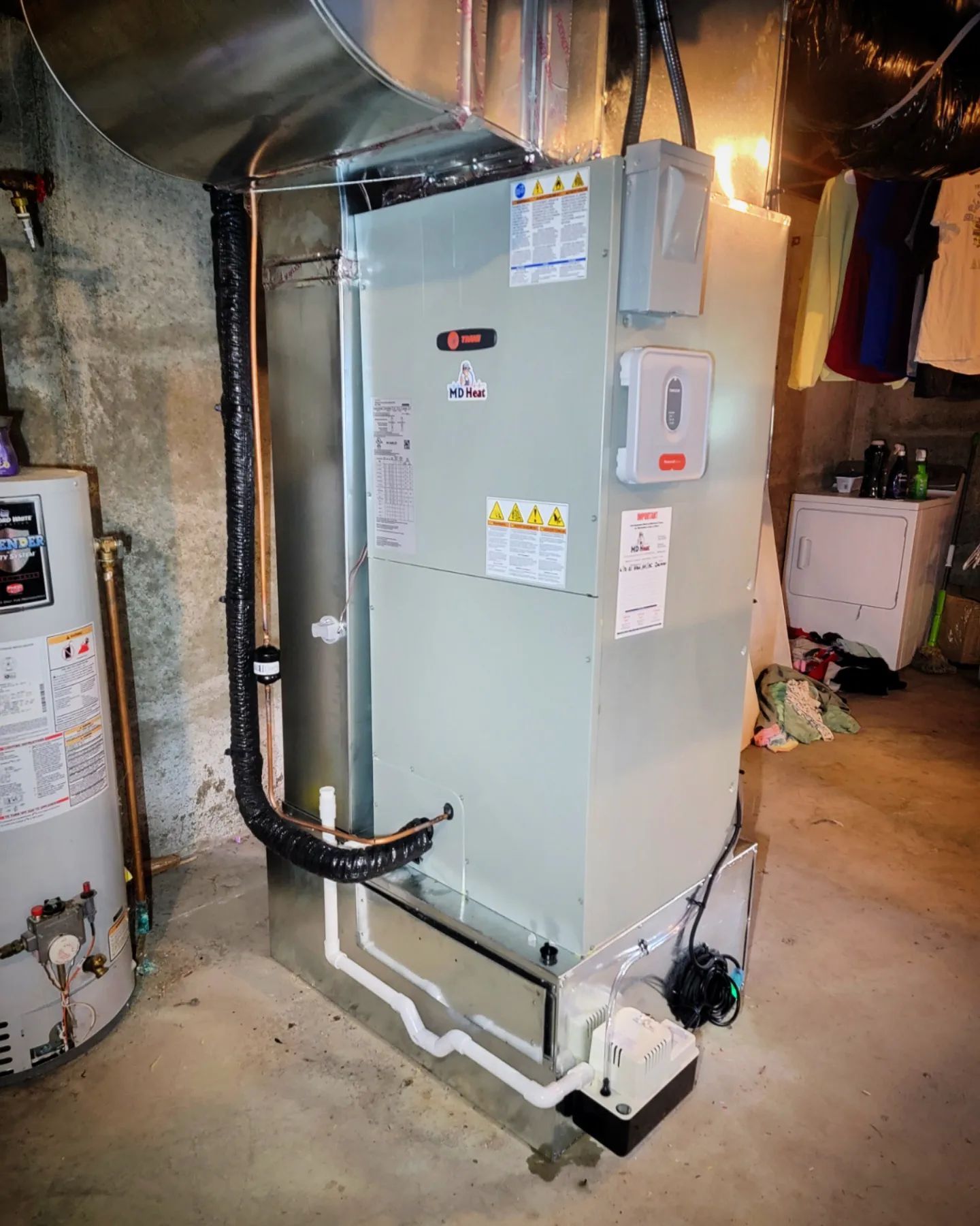 A large air conditioner is sitting in a basement next to a water heater.