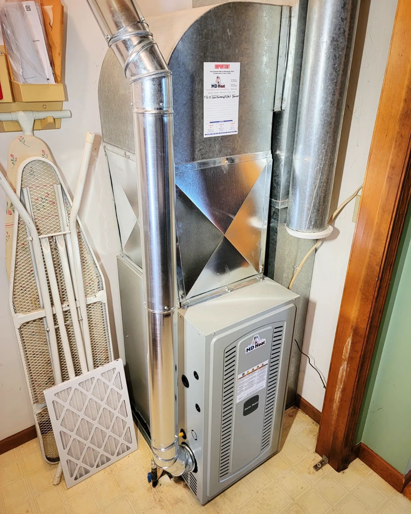 An air conditioner is sitting in a room next to an ironing board.