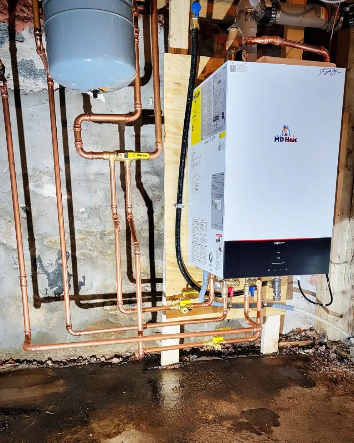A boiler is connected to copper pipes in a basement.
