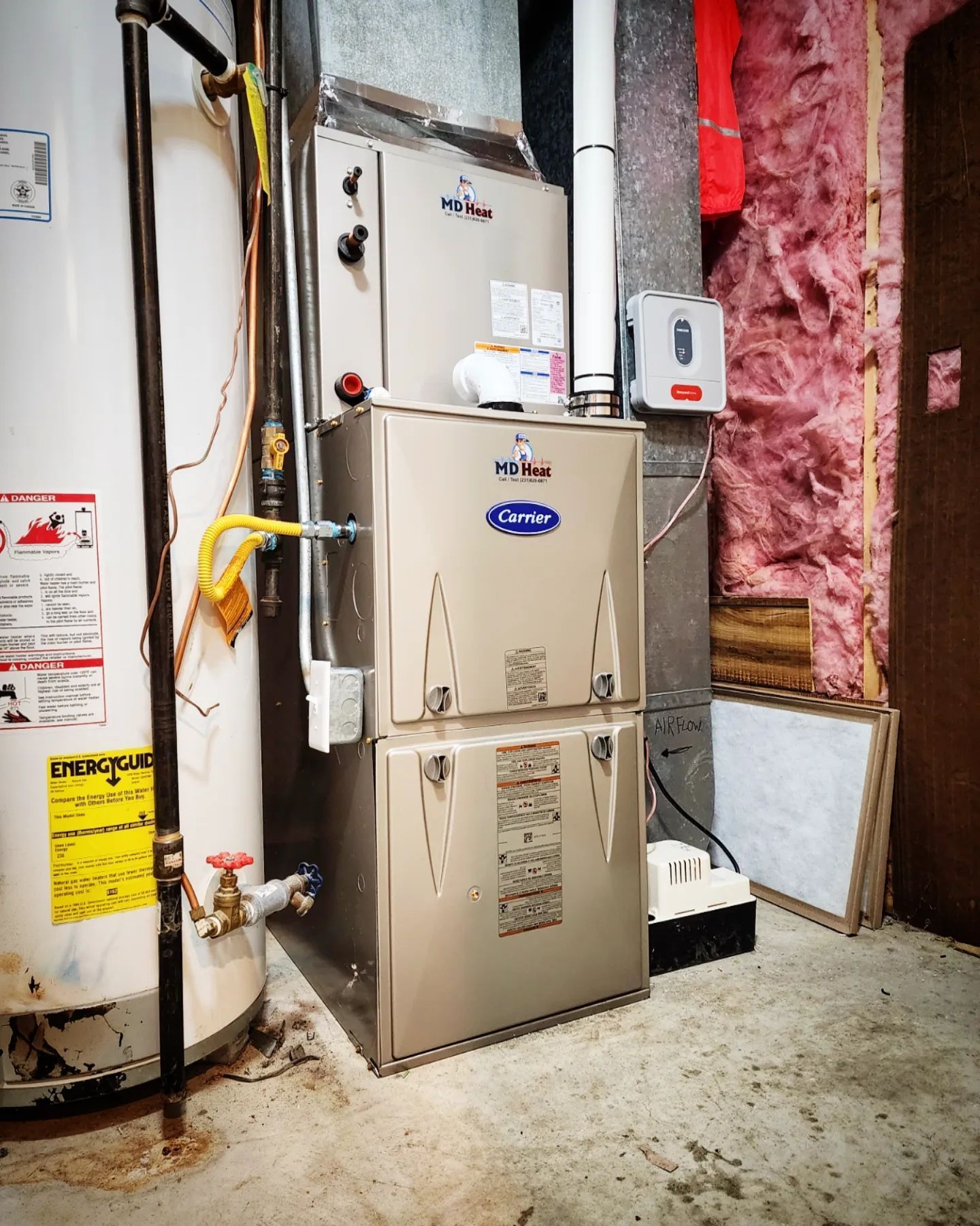A carrier furnace is sitting in a basement next to a water heater
