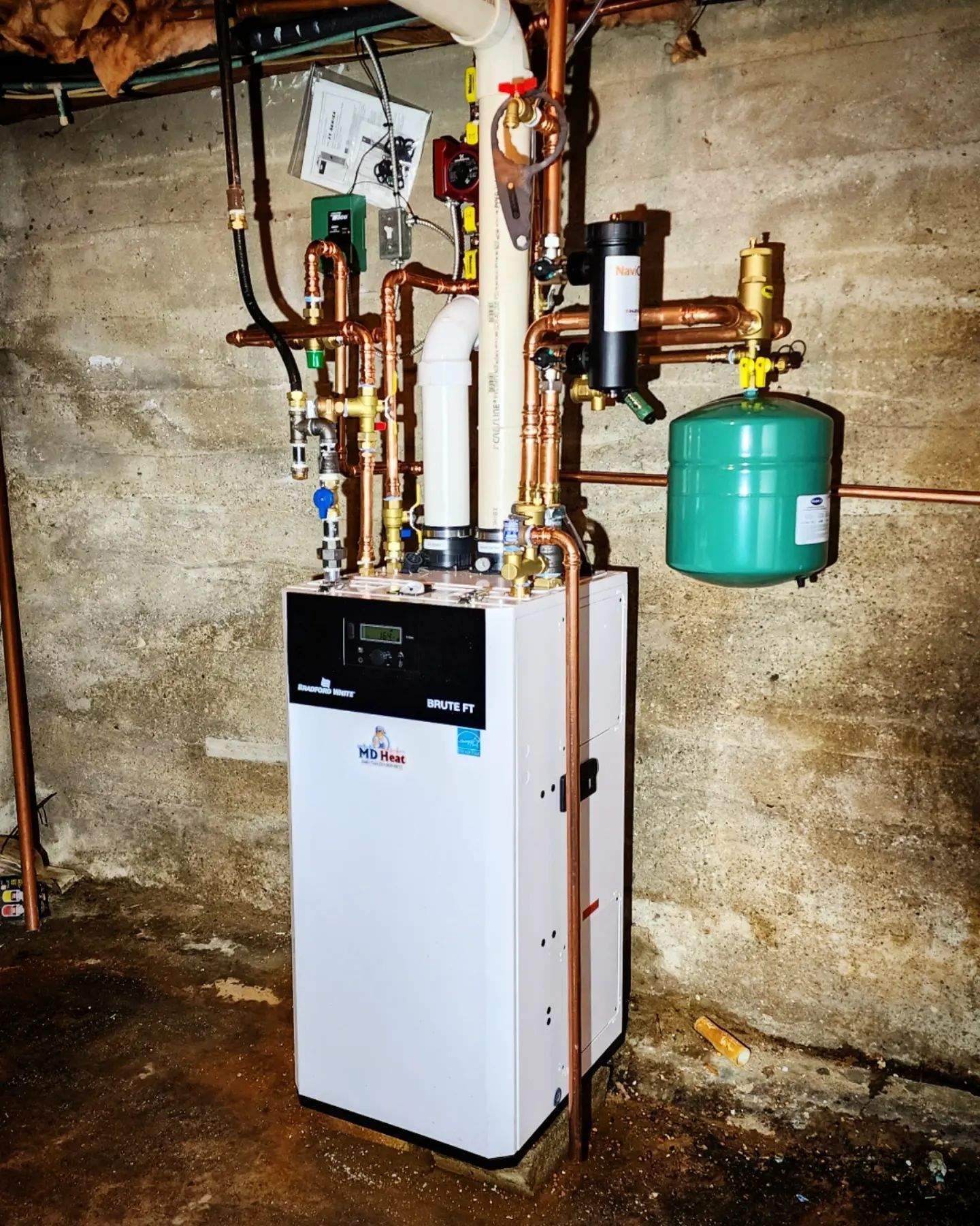 A white boiler is sitting in a basement next to copper pipes