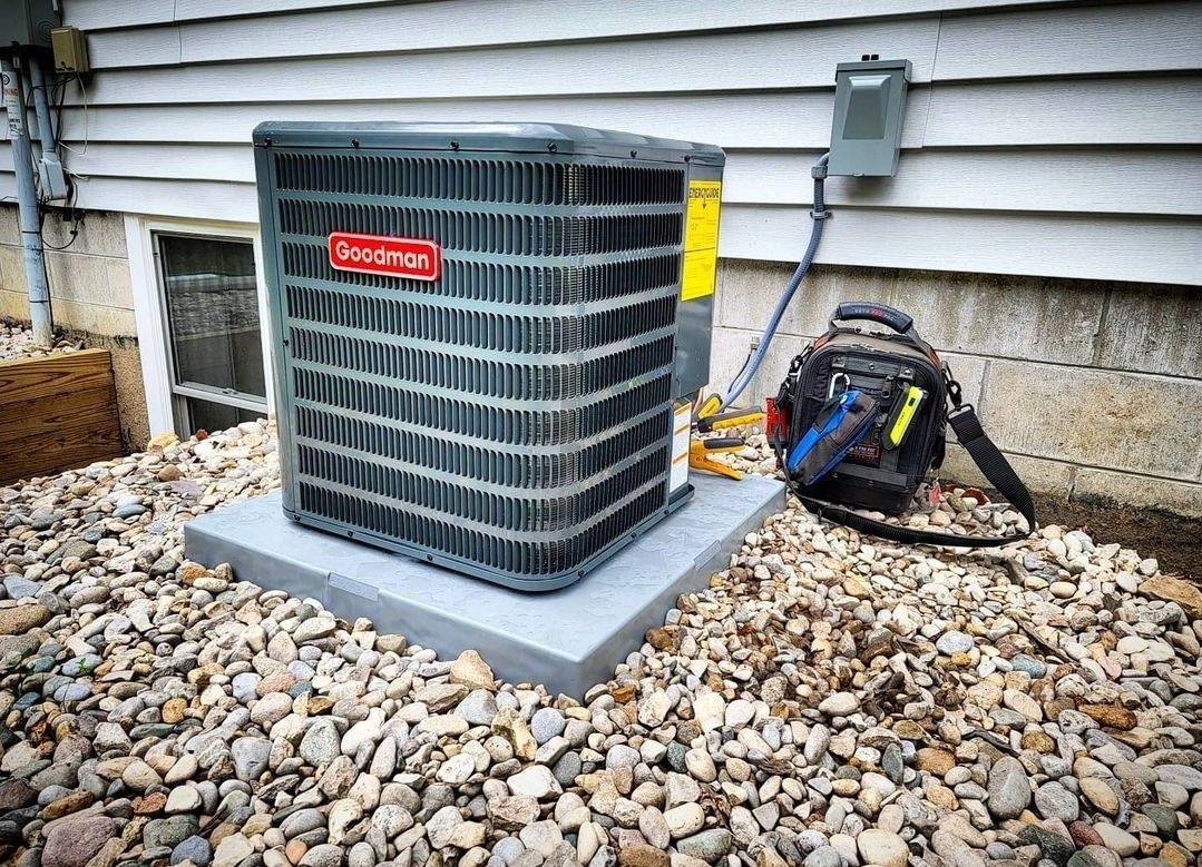 An air conditioner is sitting on top of a pile of rocks next to a house.