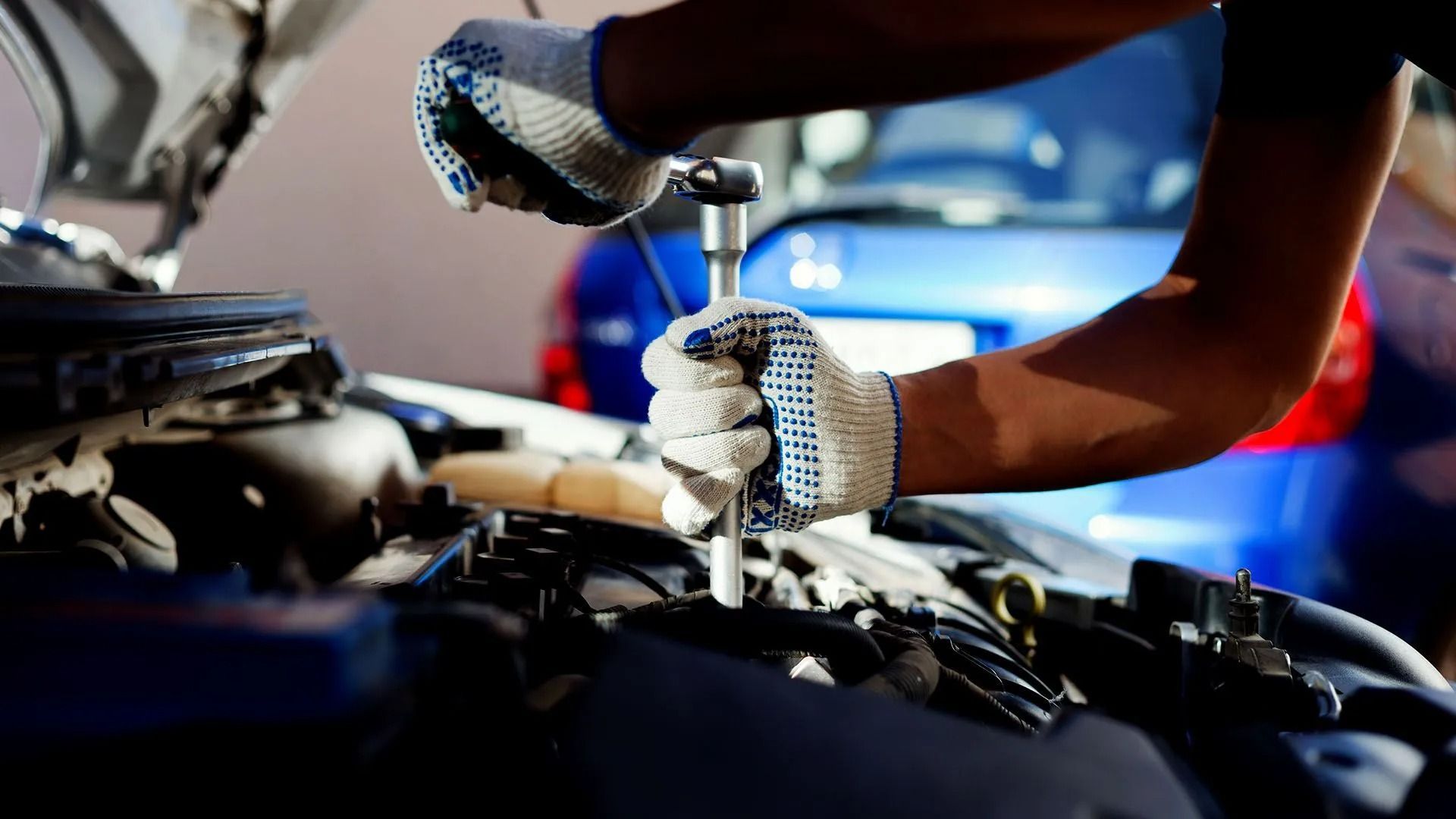 Mechanic using a wrench under the open hood of a car.