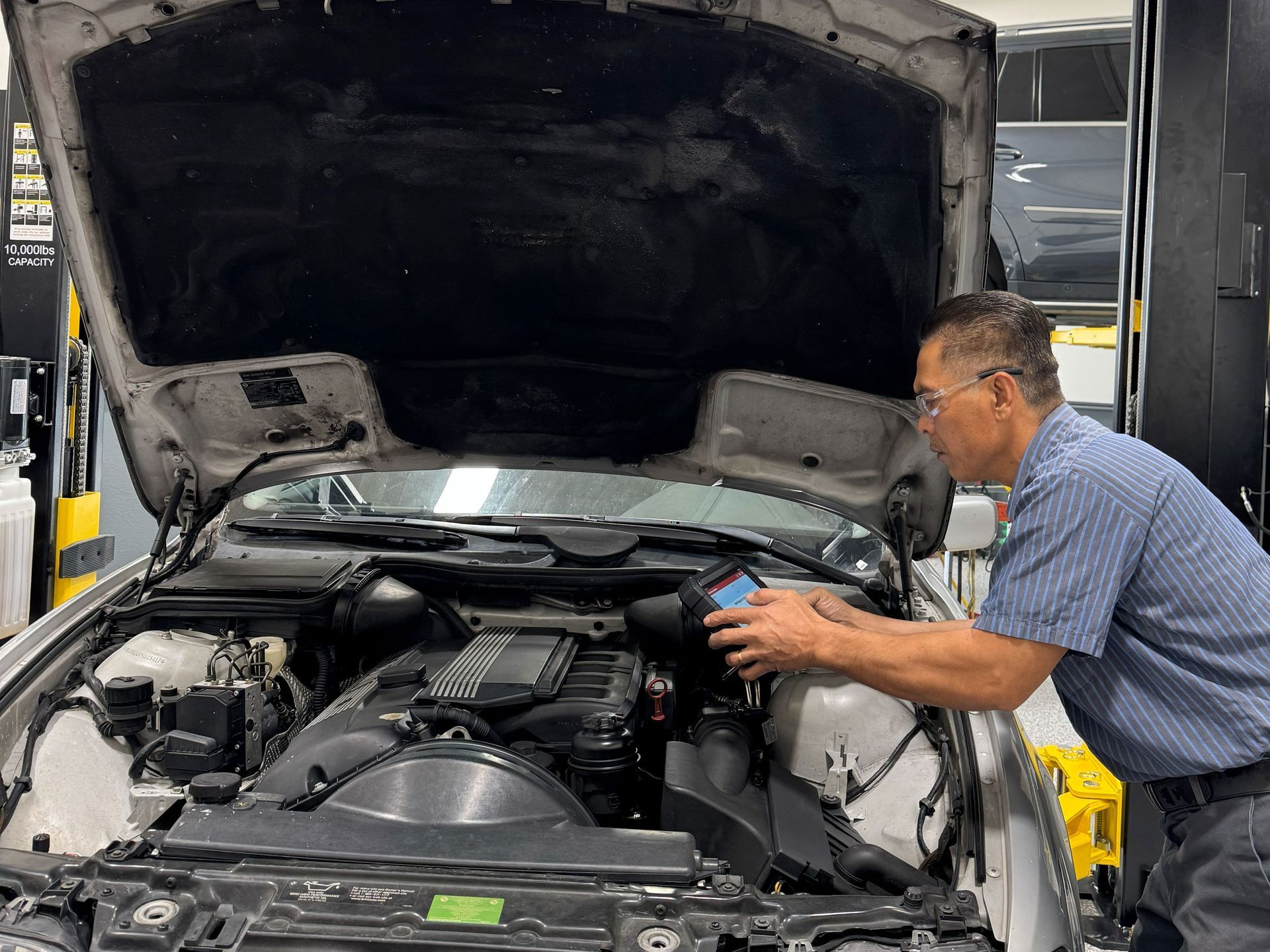 Mechanic using diagnostic tool on a car engine with the hood open. Workshop setting.