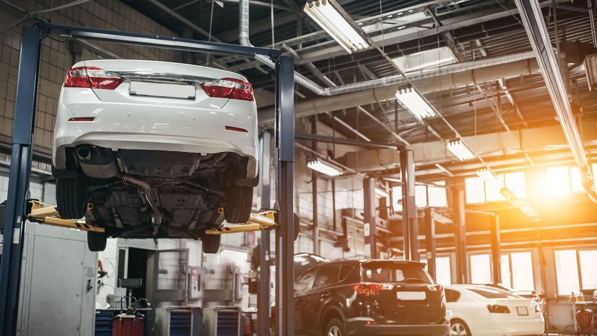 Car on a lift in a repair shop. Another car visible. Bright lighting.