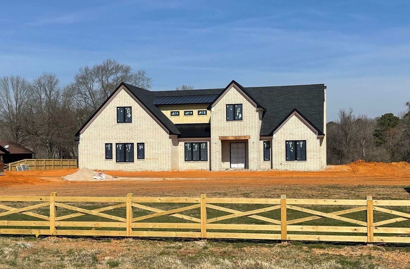 A large white house is being built in a field with a wooden fence in front of it.
