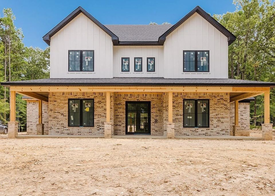Two-story white farmhouse with black trim and brick porch under construction.