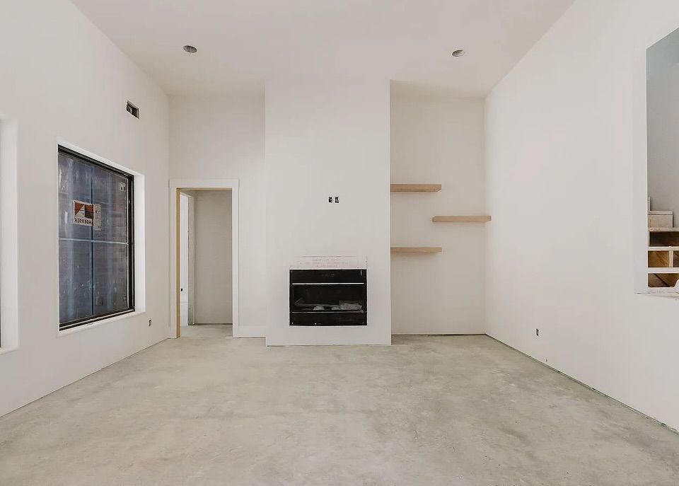 Empty living room with white walls, concrete floor, fireplace, and two wooden shelves.
