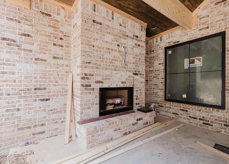 Brick fireplace with a black framed window in a partially constructed room.