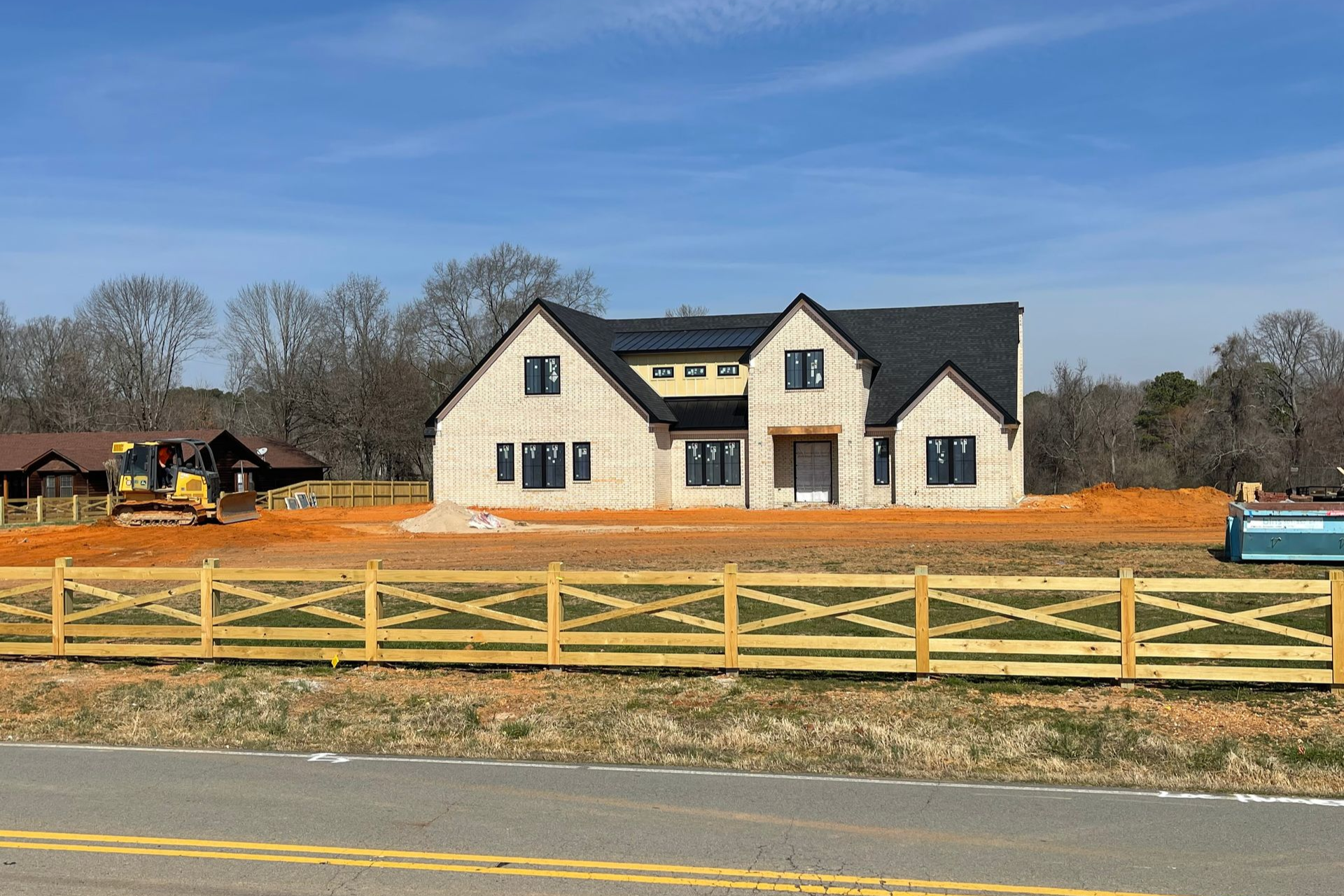A large white house is being built in a field with a wooden fence in front of it.