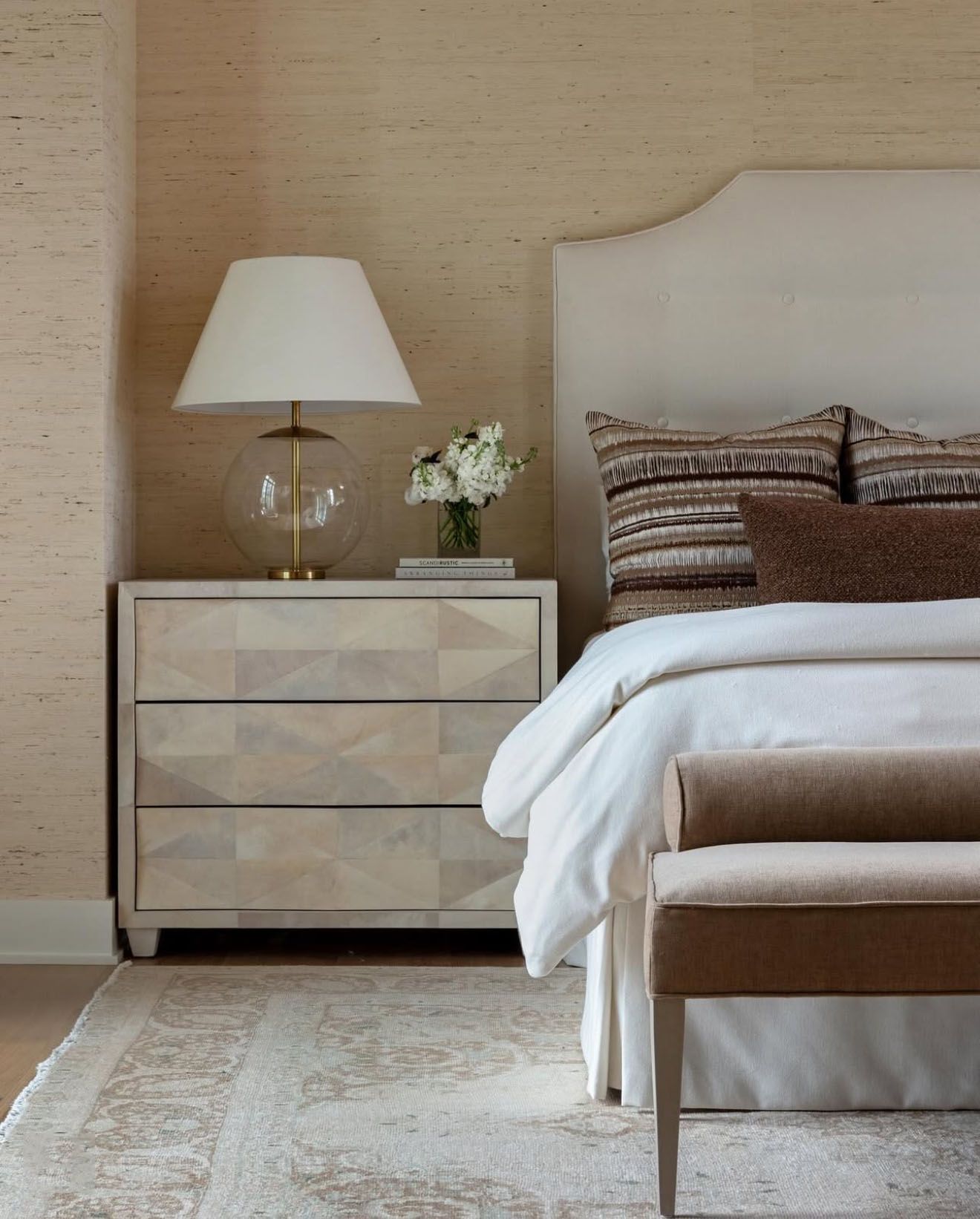 A bedroom with a bed a nightstand a lamp and a bench