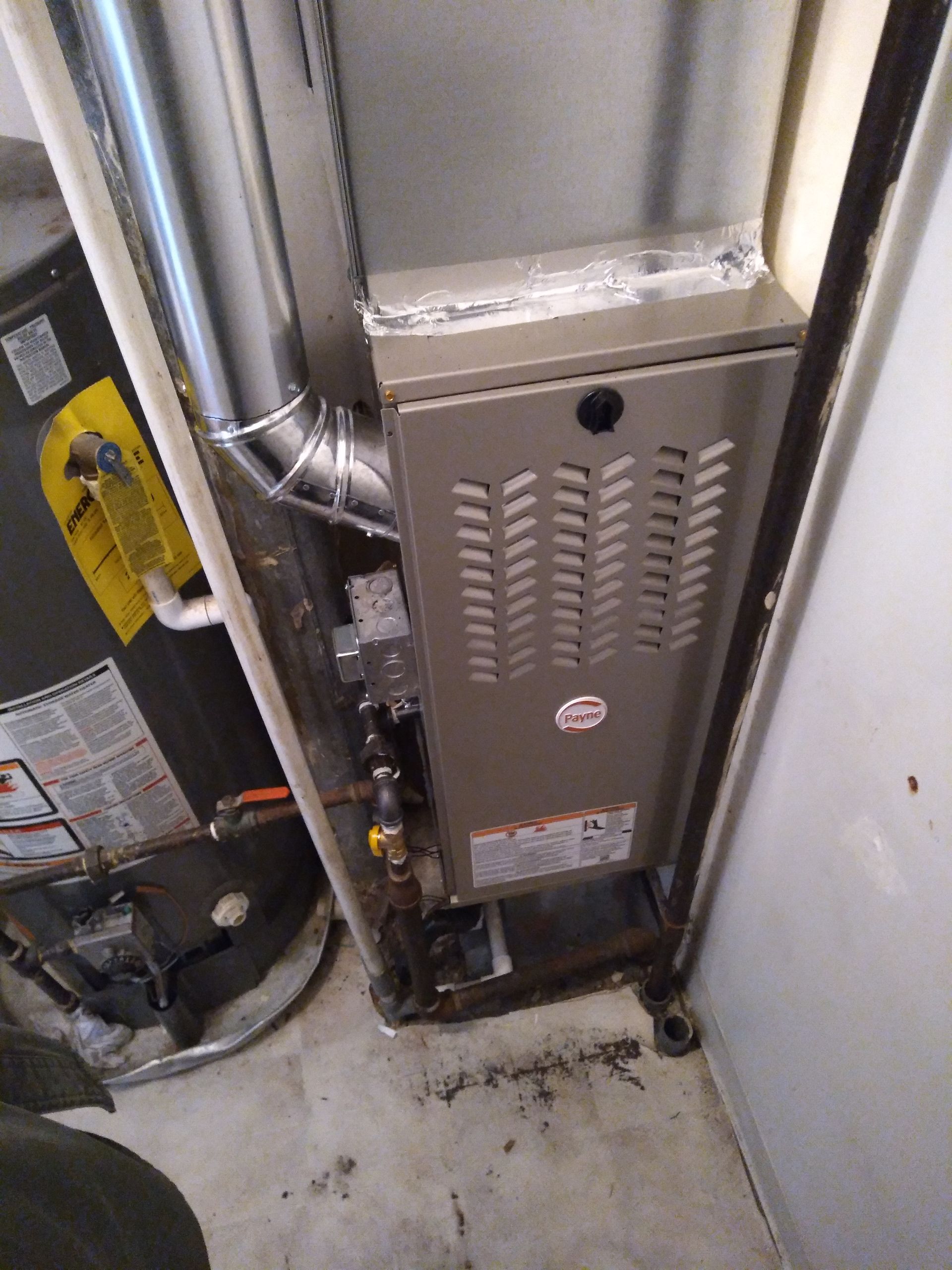 A furnace is sitting in a room next to a water heater.