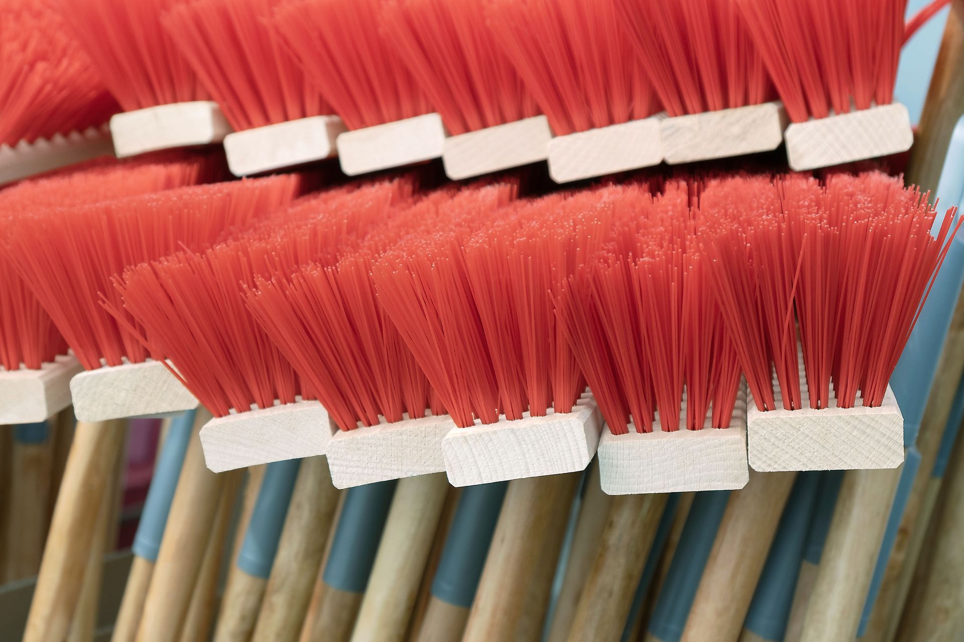Close-up of red-bristled brooms with white bristle holders and wooden handles stacked together.