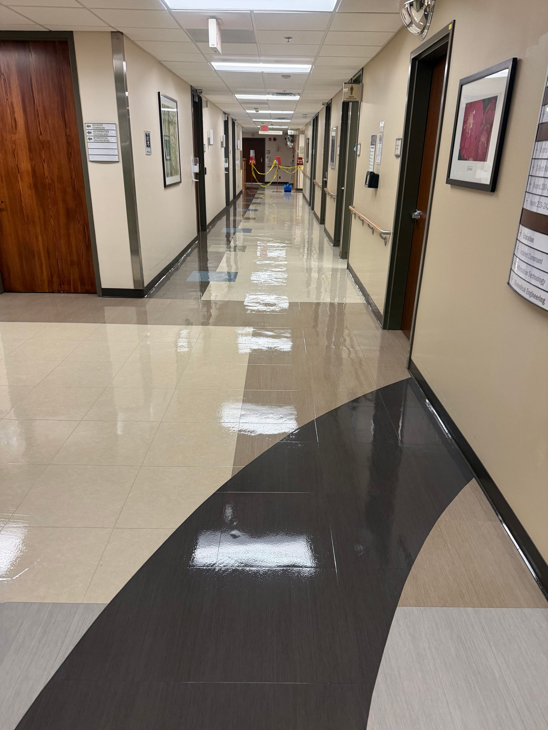 Empty indoor hallway with glossy tiled floor, framed wall art, and office doors on both sides.
