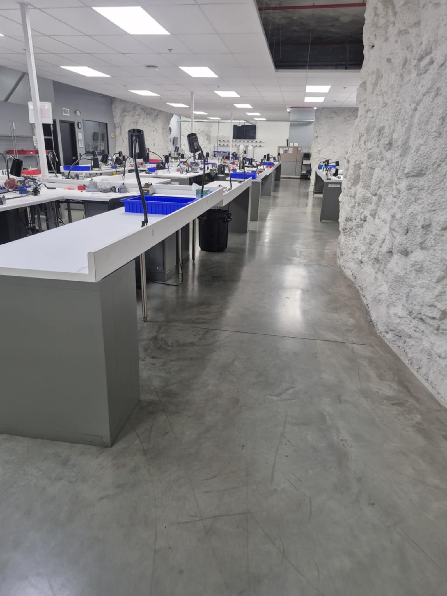 Bright sewing workshop with long tables, overhead lights, and a polished concrete floor.