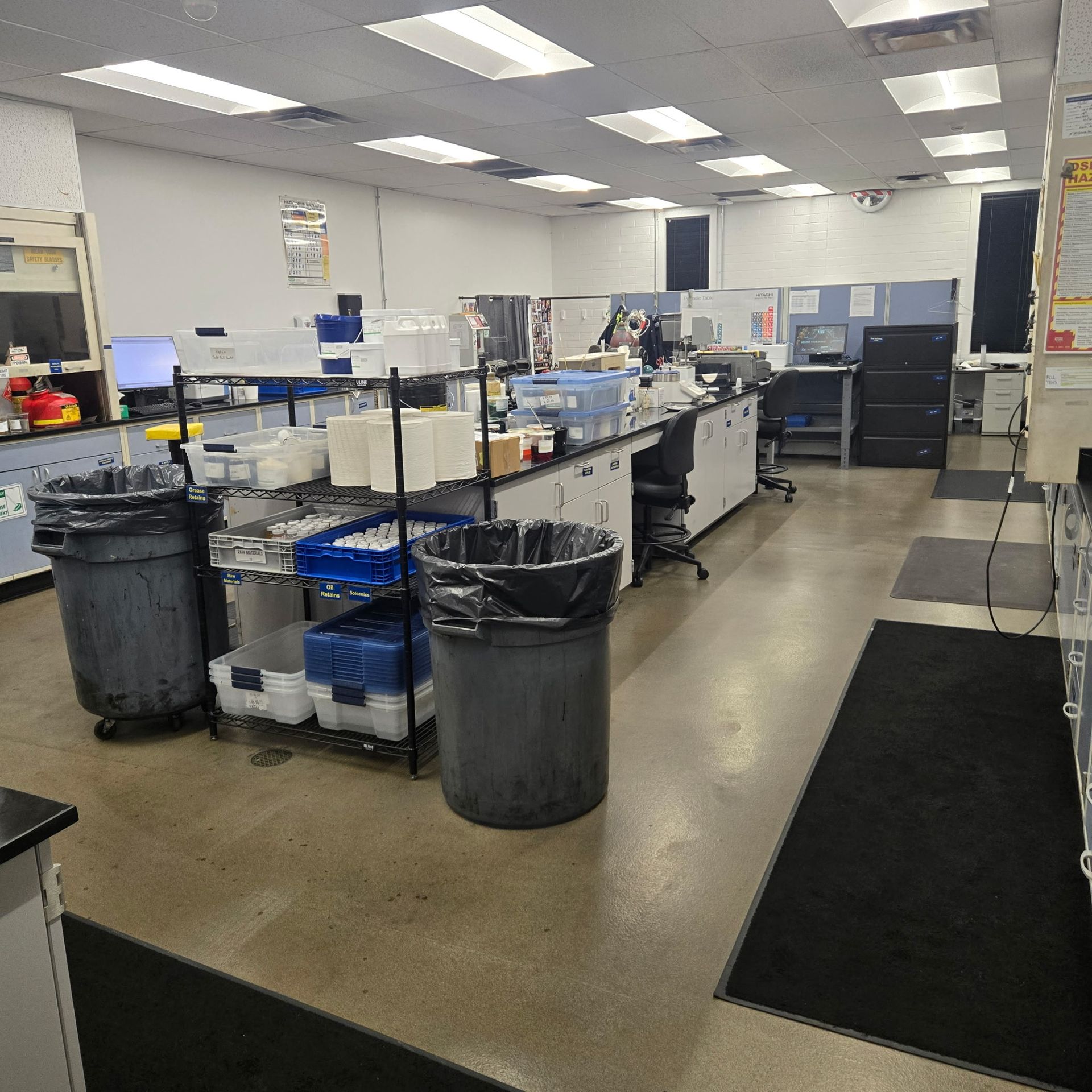 Laboratory workspace with benches, equipment, trash bins, and black floor mats