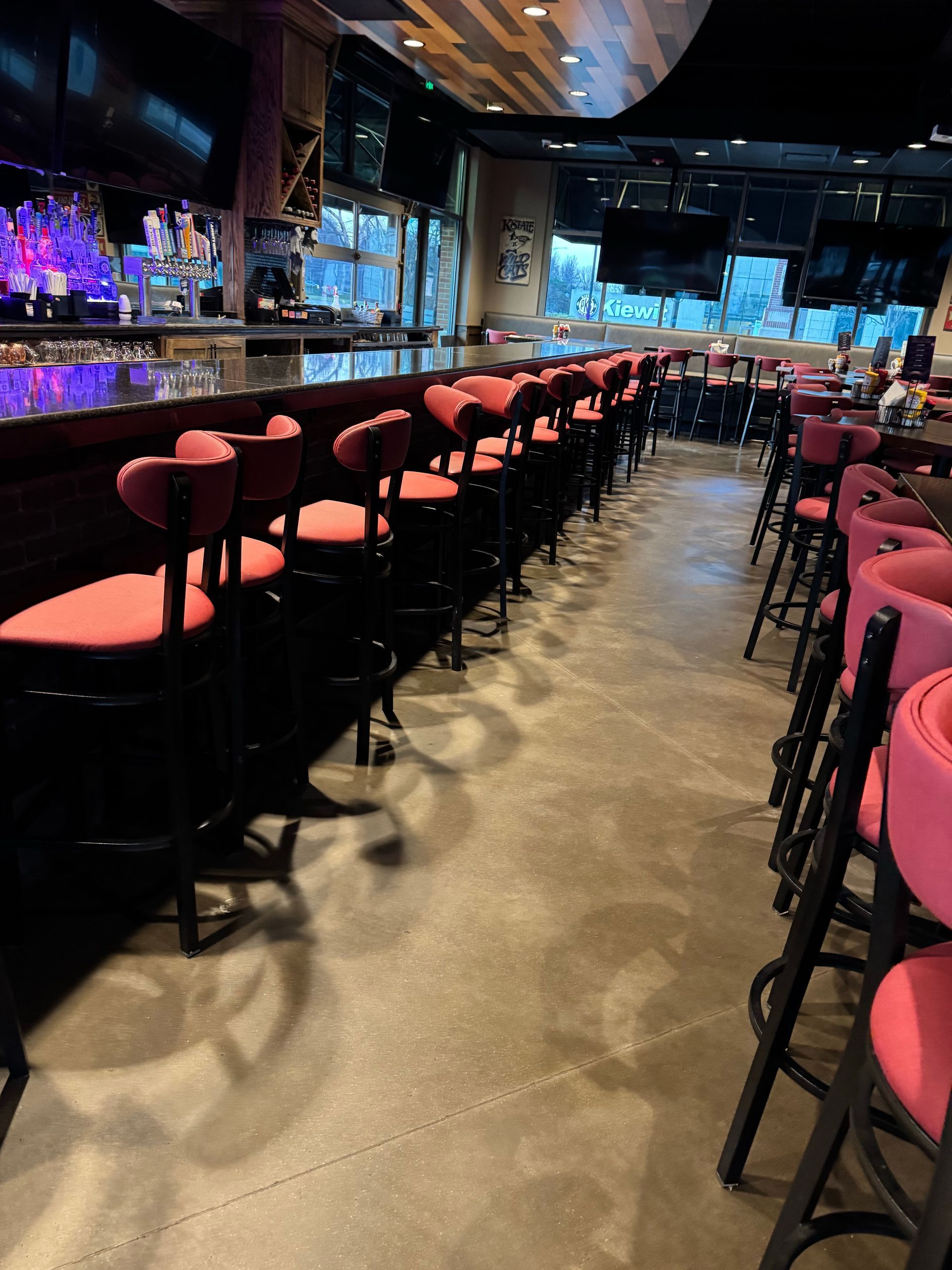 Empty bar with red stools lining both sides of a polished floor, dimly lit with a blue-lit back wall