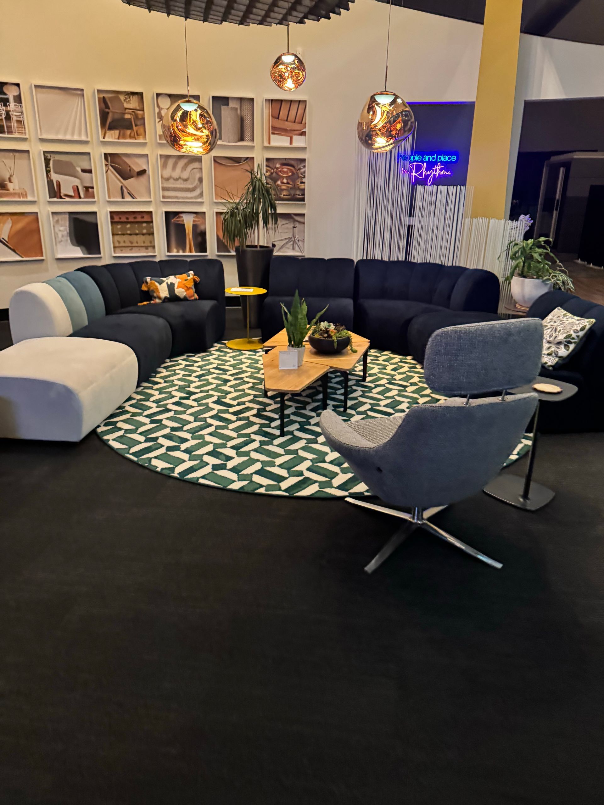Modern lounge with curved dark sofas, patterned rug, round table, and hanging pendant lights.
