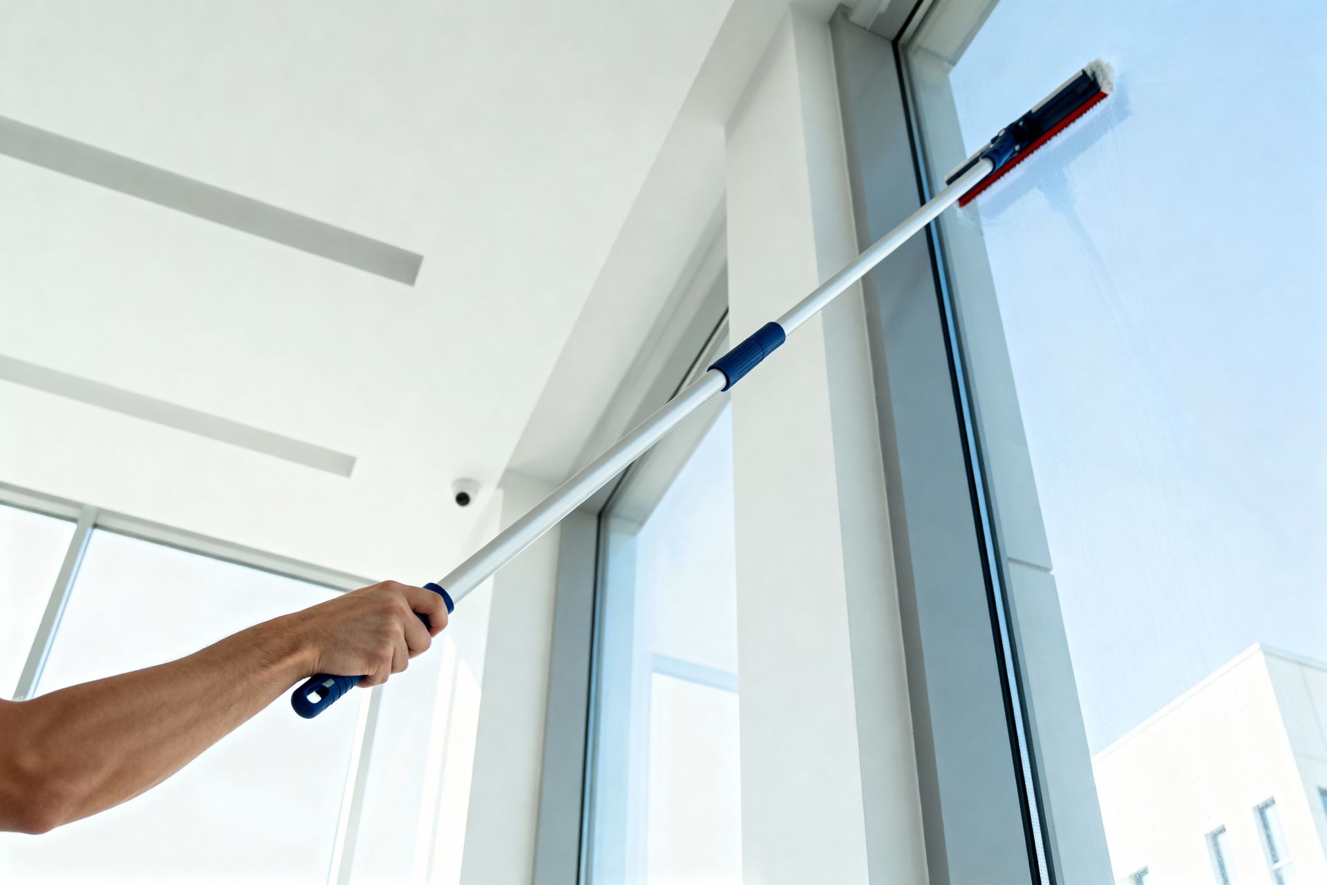 Person using a long-handled squeegee to clean tall glass windows indoors