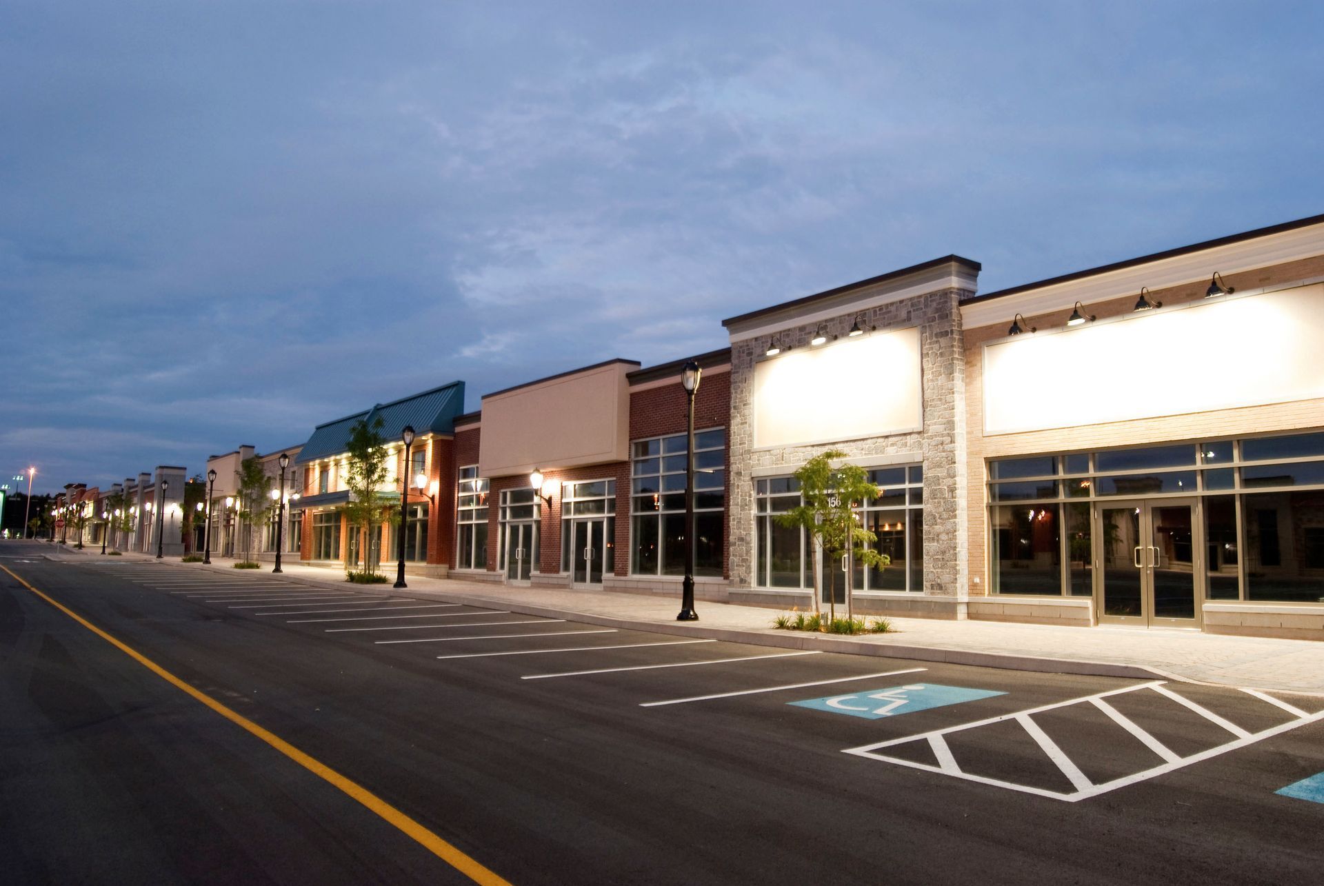 Empty shopping strip mall at dusk with lit storefronts and empty parking lot