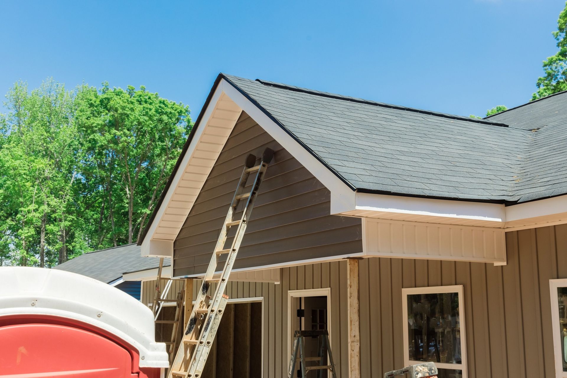 House under construction with ladder against the side, brown siding, dark roof, blue sky.