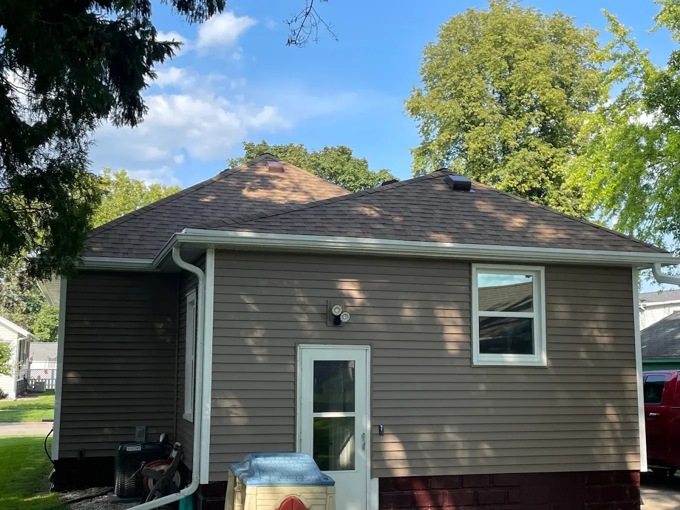 Tan house with brown roof, white trim, and a small yard on a sunny day.