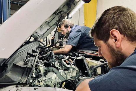 Two men are working on a car engine in a garage.