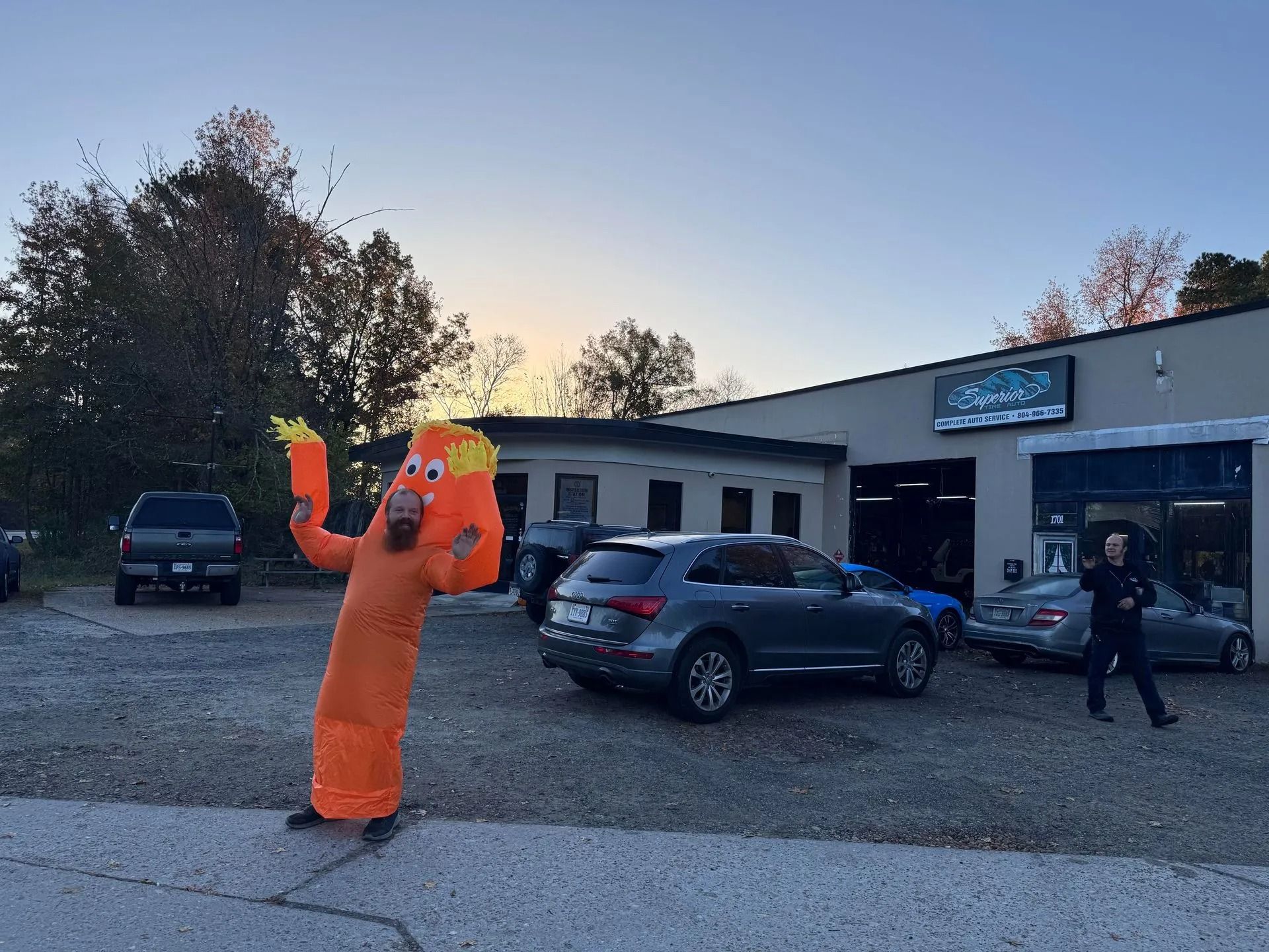 Orange inflatable tube man waving in front of a car repair shop. Cars parked outside.