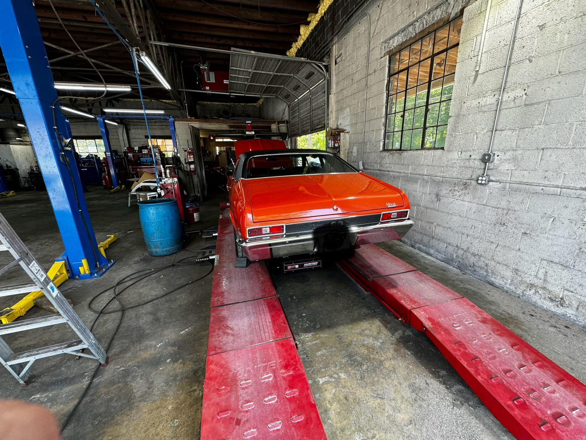 Orange classic car on a red lift in a garage, facing away.