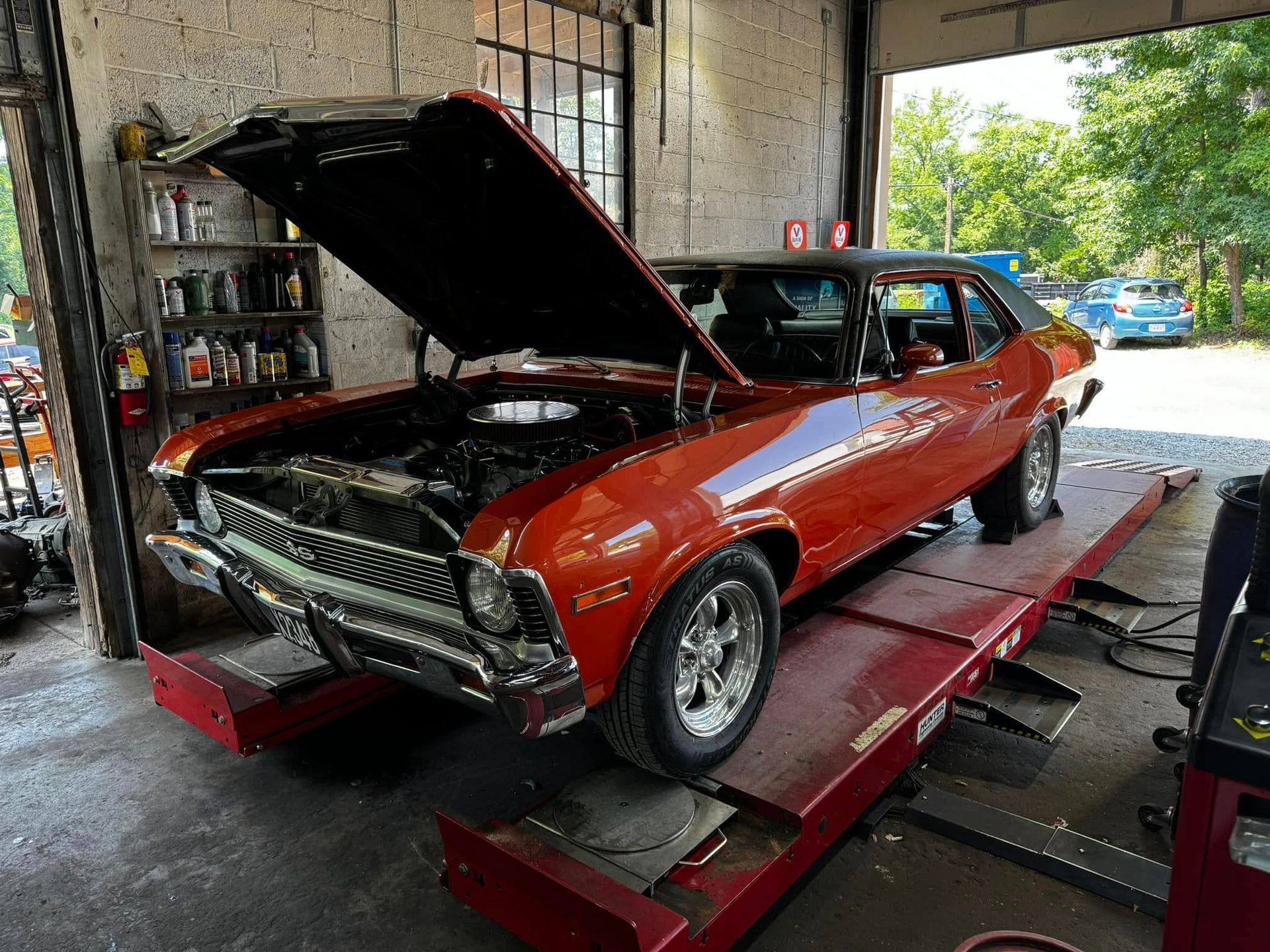 Classic orange car with black roof on a lift inside a garage, hood open.