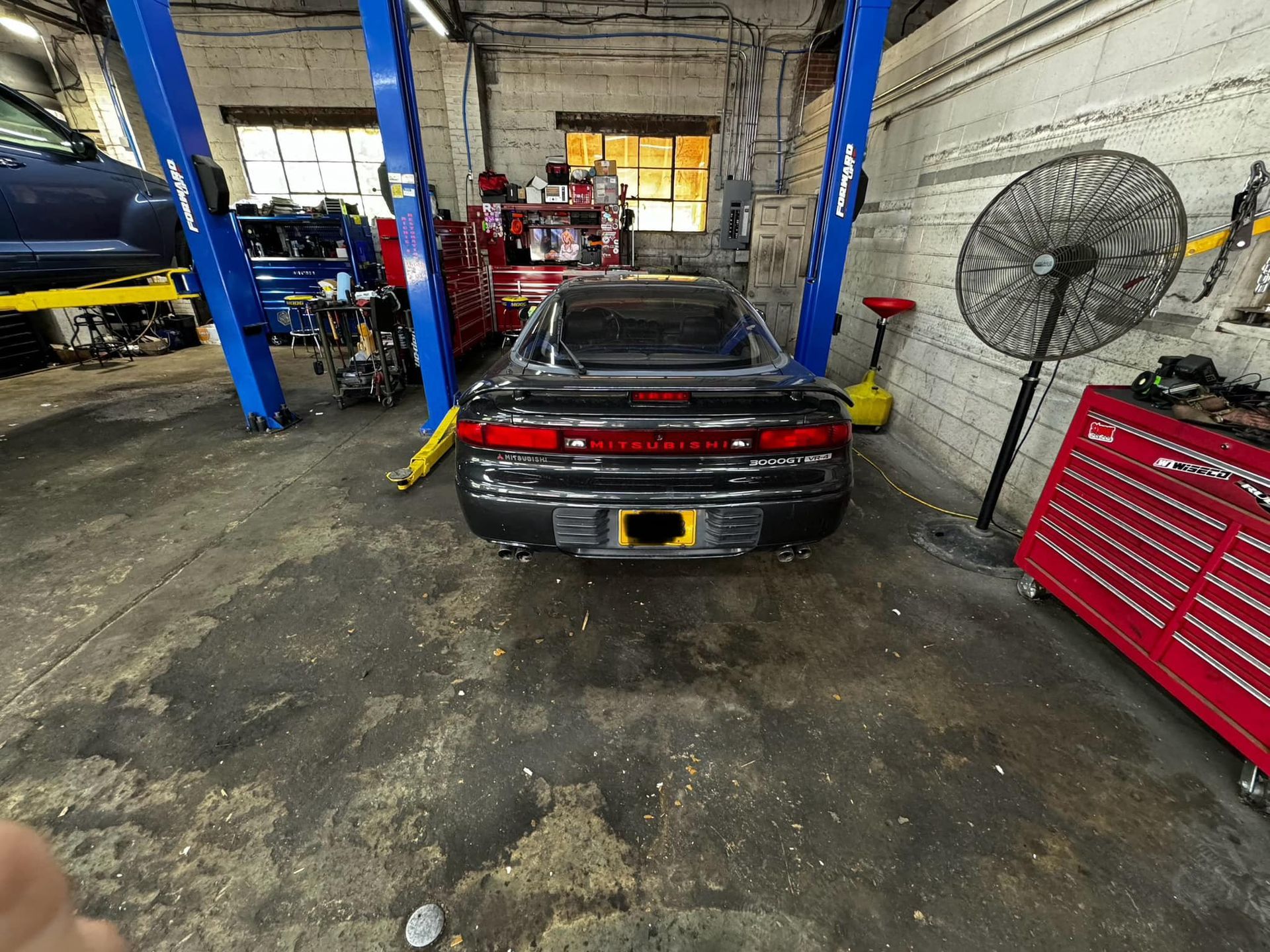 Black sports car inside a garage, with blue car lift and tool chest.