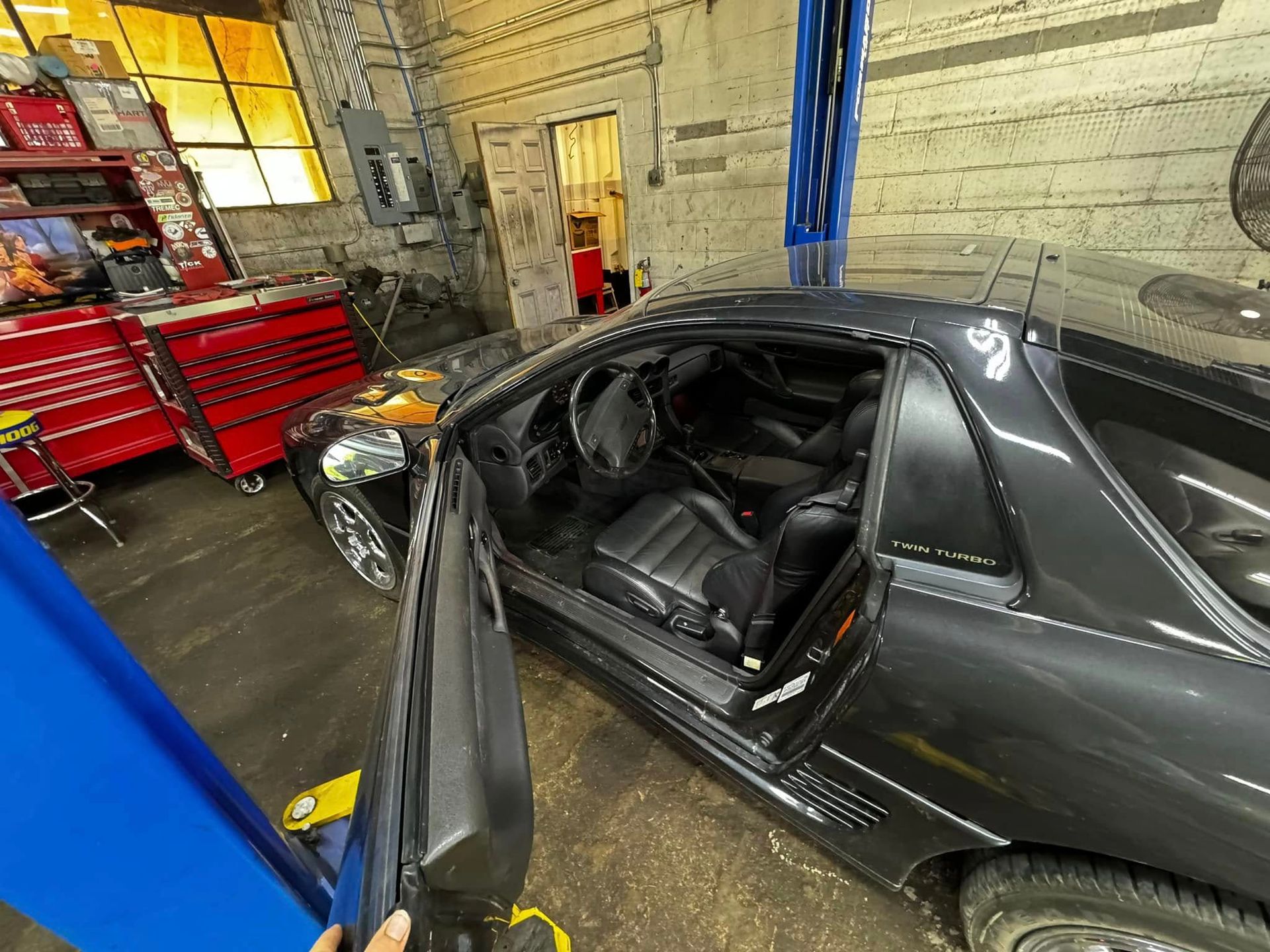 Black sports car with door open in a garage, revealing interior.