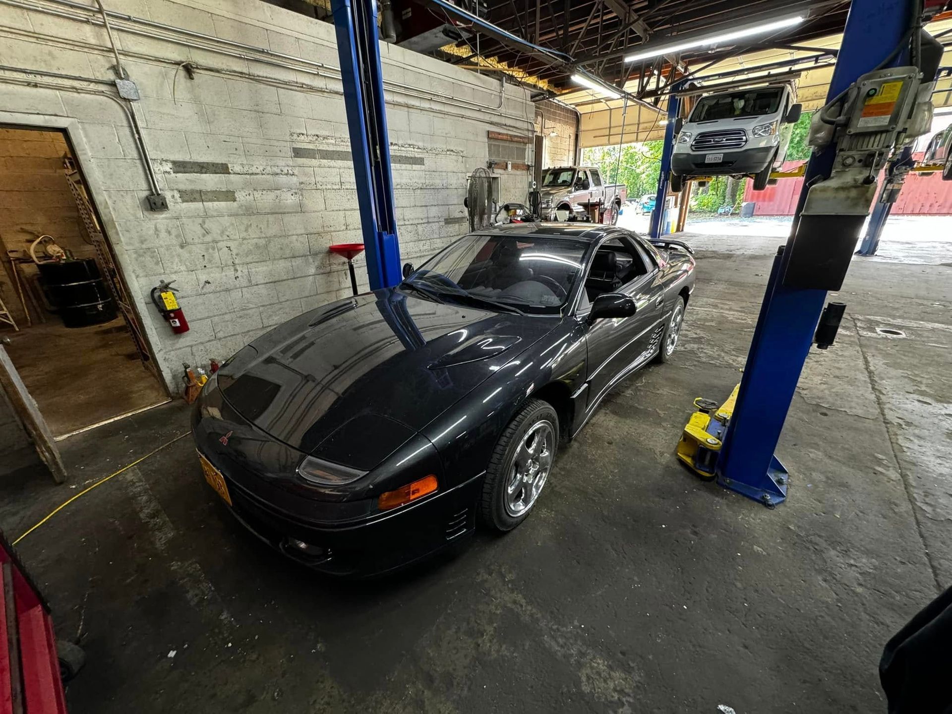 Dark car raised on a blue lift in a garage, another vehicle in background.