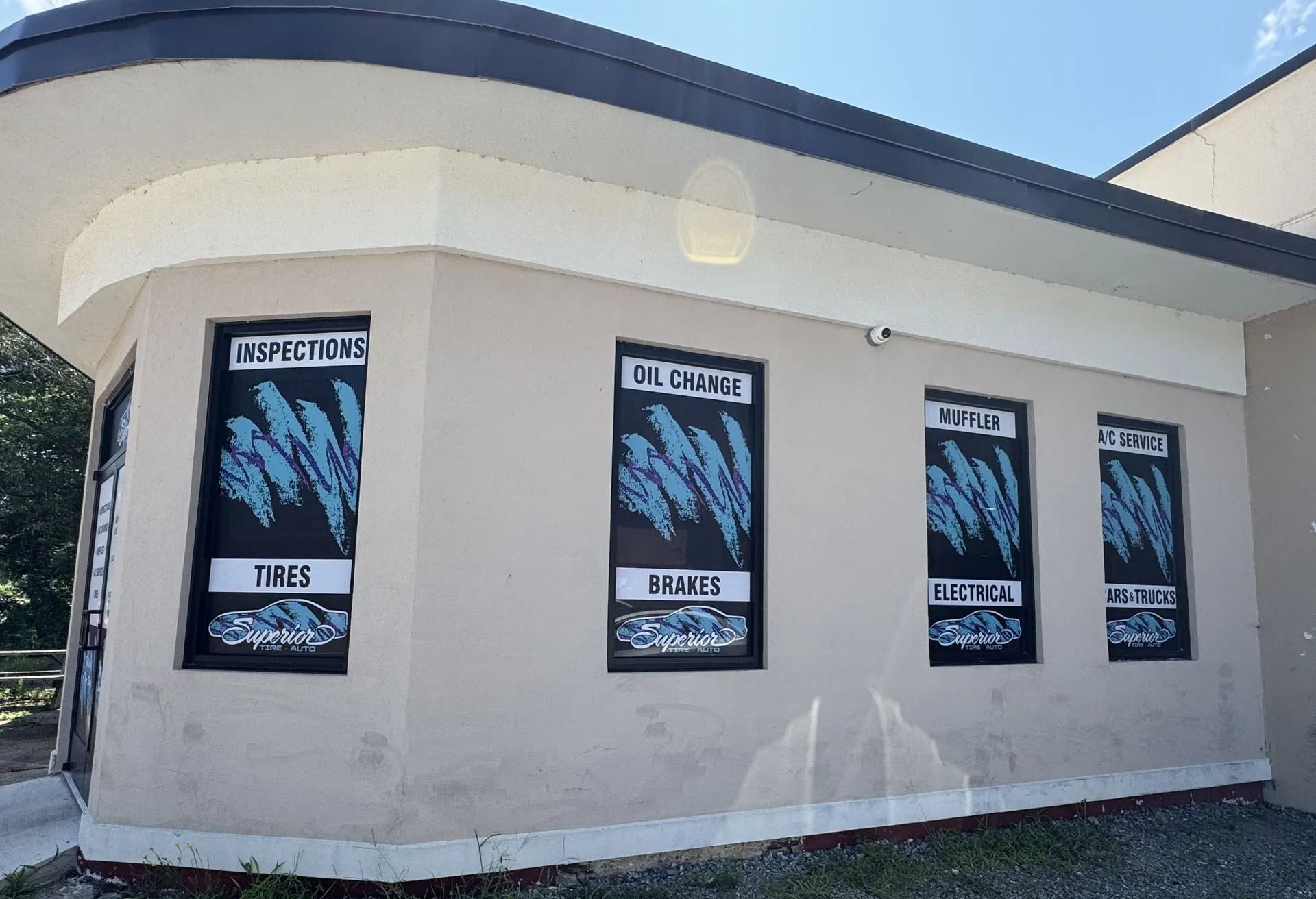 Exterior of a beige auto shop with signs for inspection, oil change, brakes, and tires.