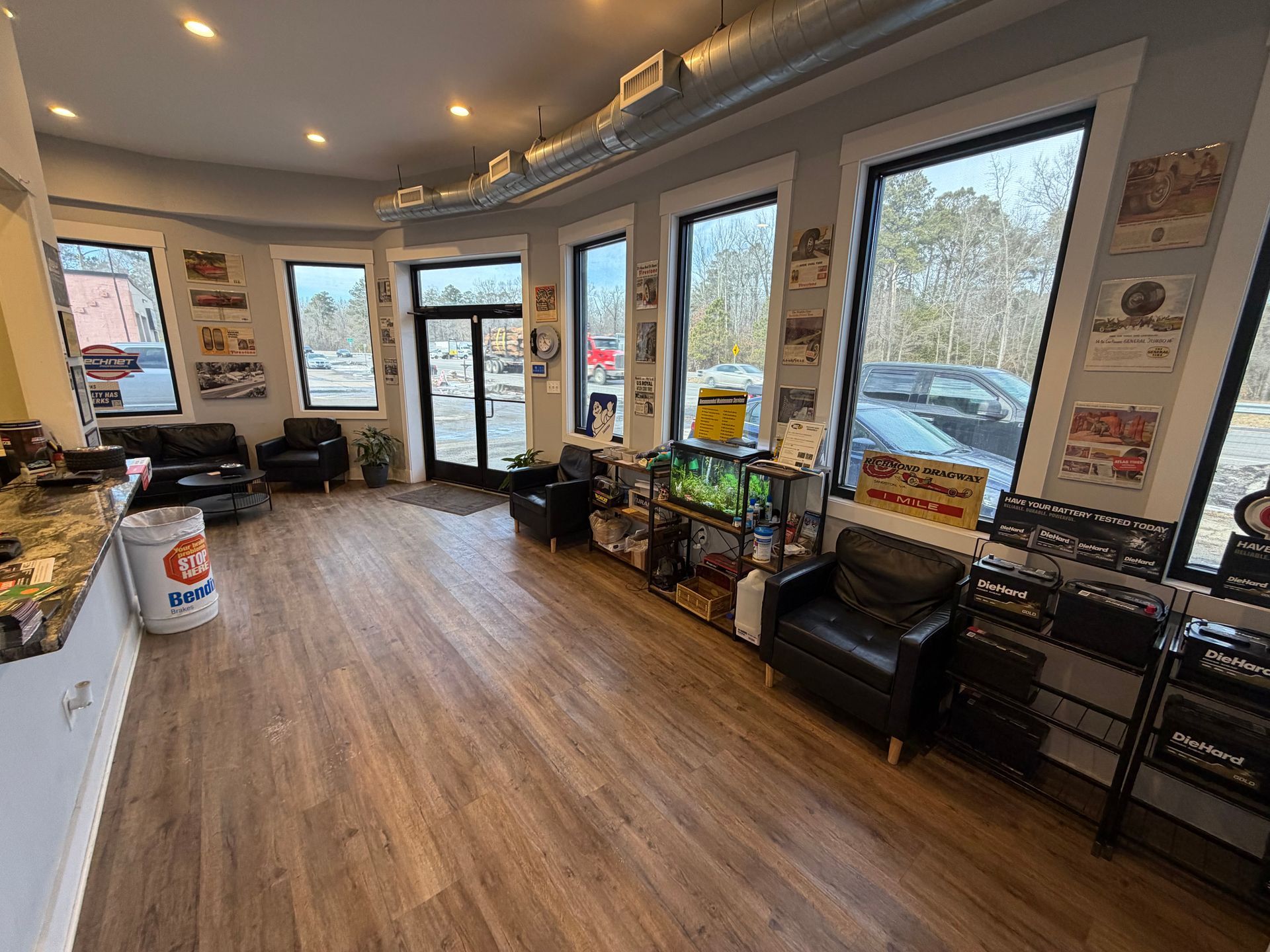 Waiting area in auto shop with black chairs, a fish tank, and display items by windows.