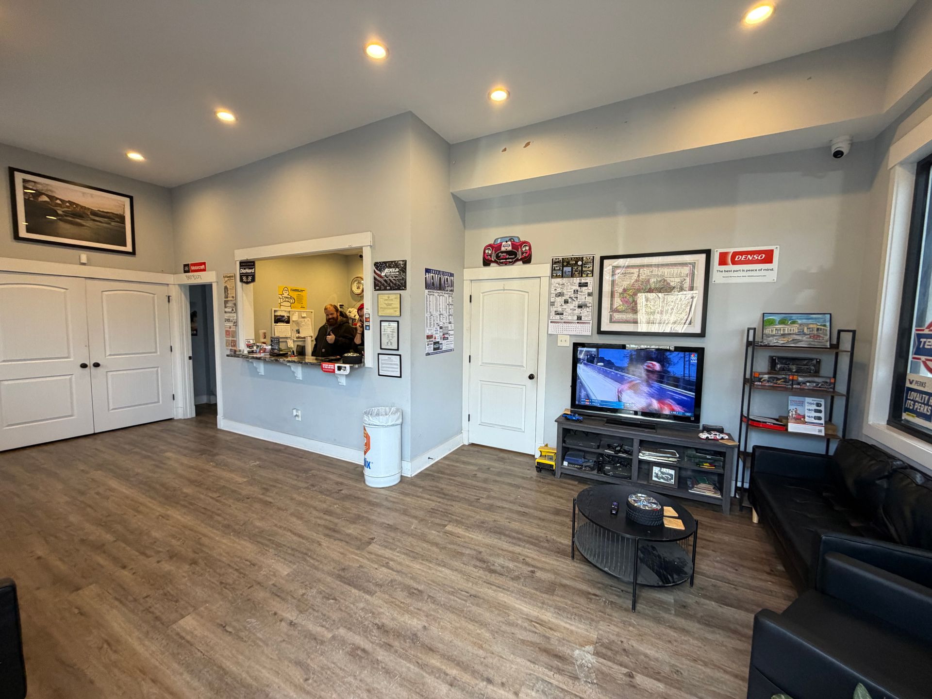 Auto repair shop waiting area with counter, TV, black sofa, and wood-look flooring.
