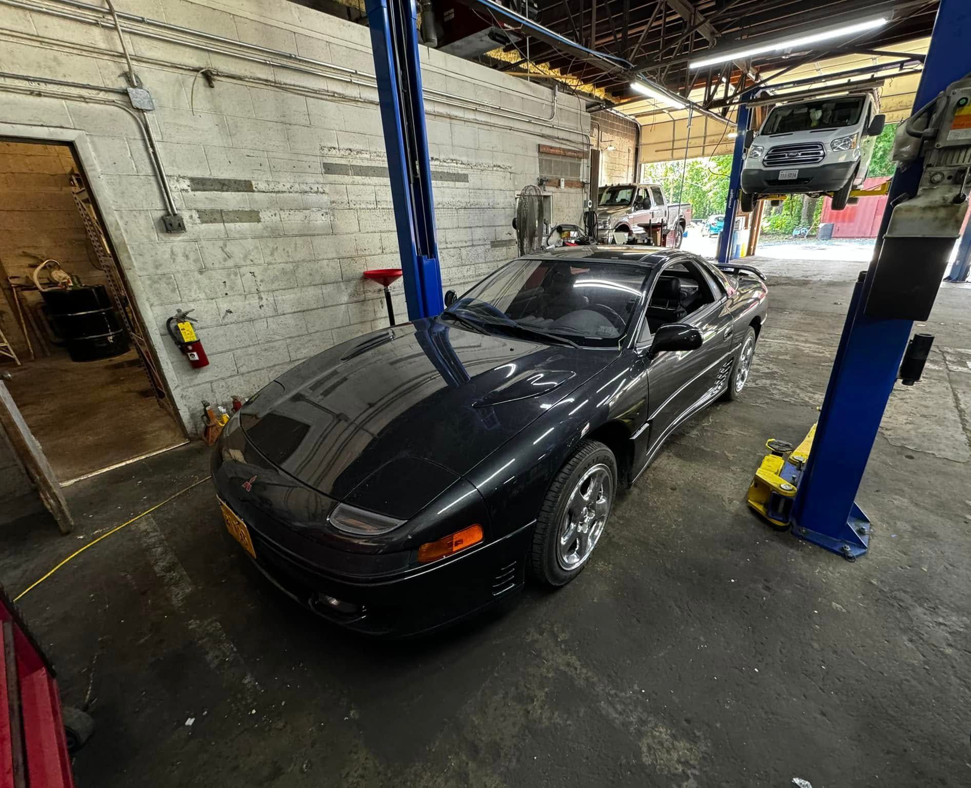 Black sports car in a garage with a car lift, another vehicle in the background.