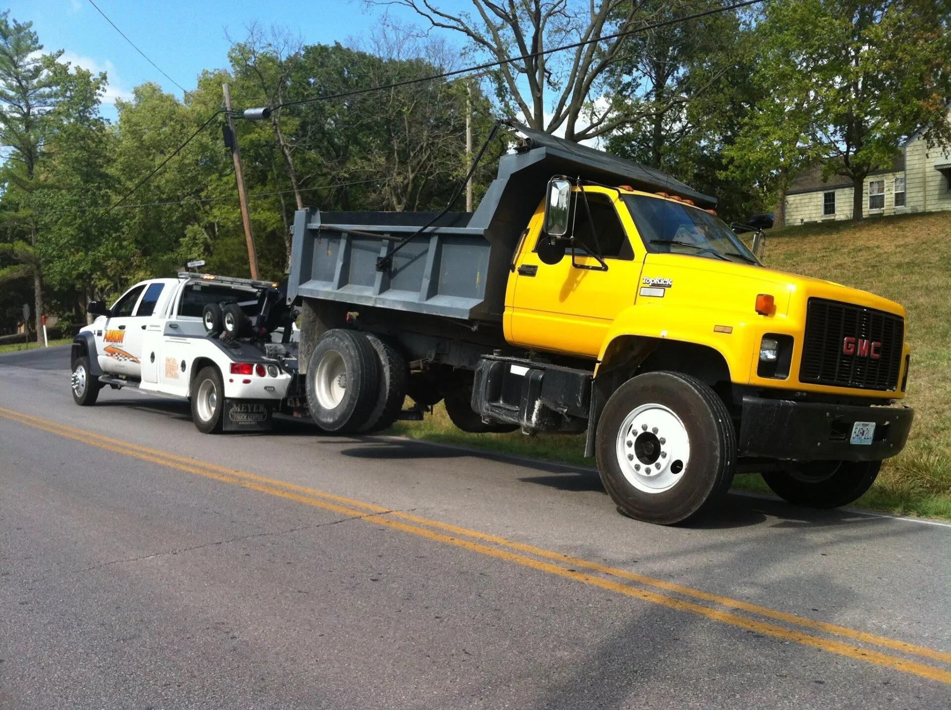 A yellow dump truck being towed by a white tow truck on a road.